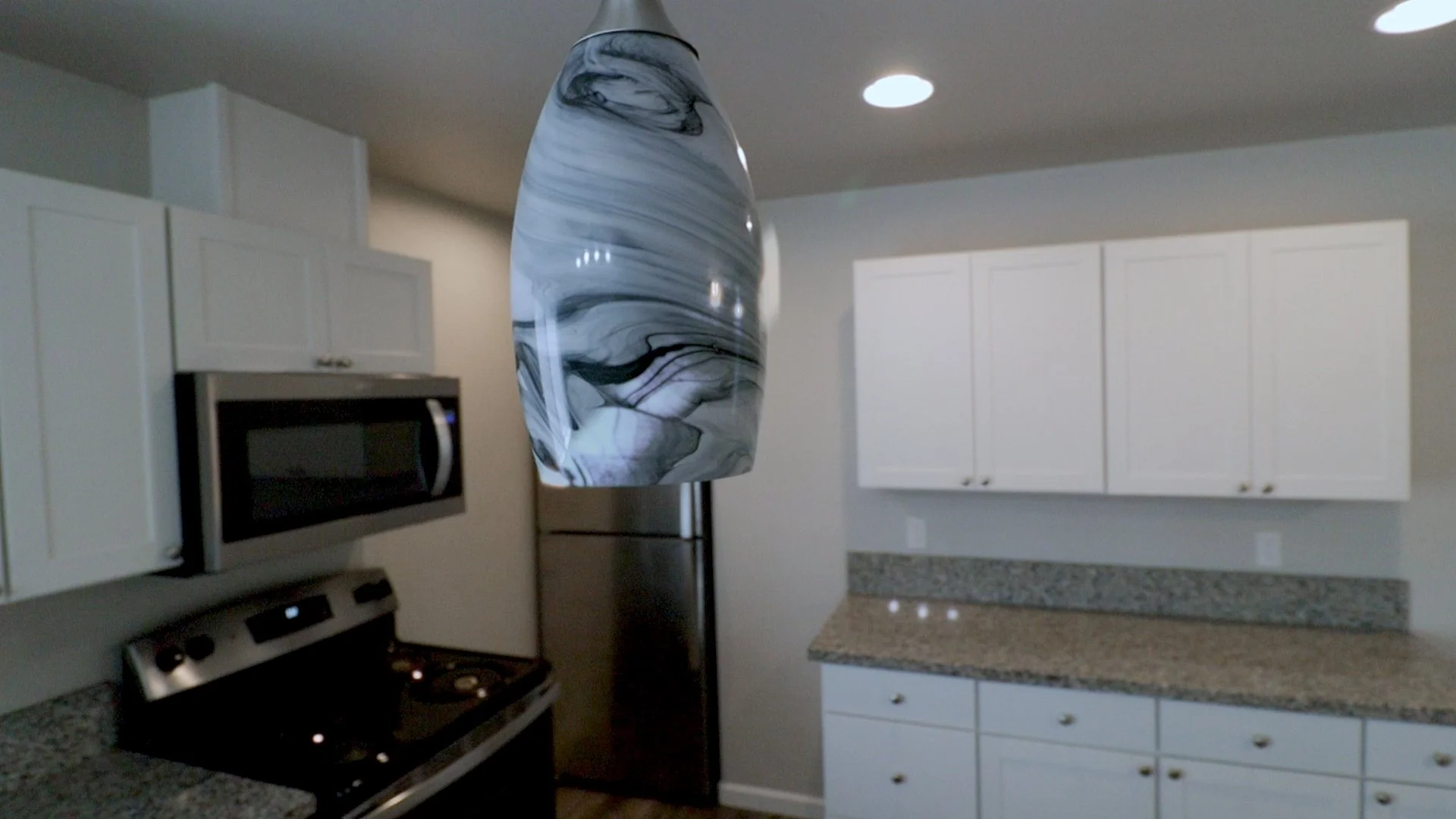 Modern kitchen with white cabinets, granite countertops, stainless steel appliances, and a marble-patterned pendant light.