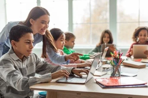 Teacher and students in a classroom using laptops and tablets.