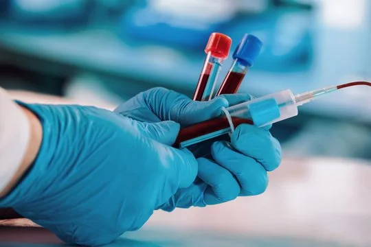 Person wearing blue gloves holding test tubes with blood samples and a pipette.