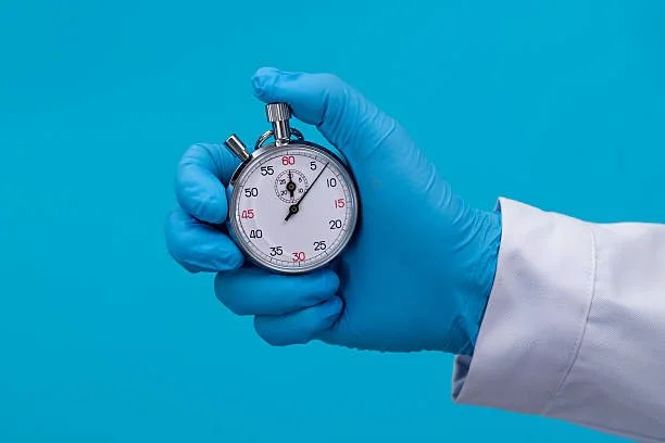Person wearing a blue glove holding a stopwatch against a blue background.