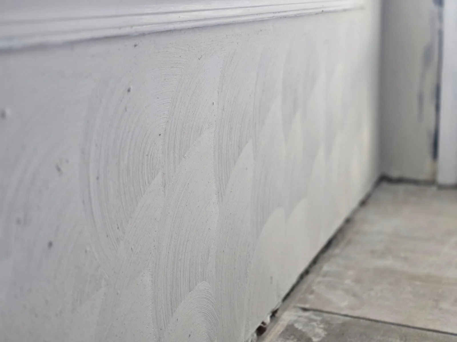 Close-up of a textured white wall with visible plaster brush strokes and a corner where the wall meets the floor.