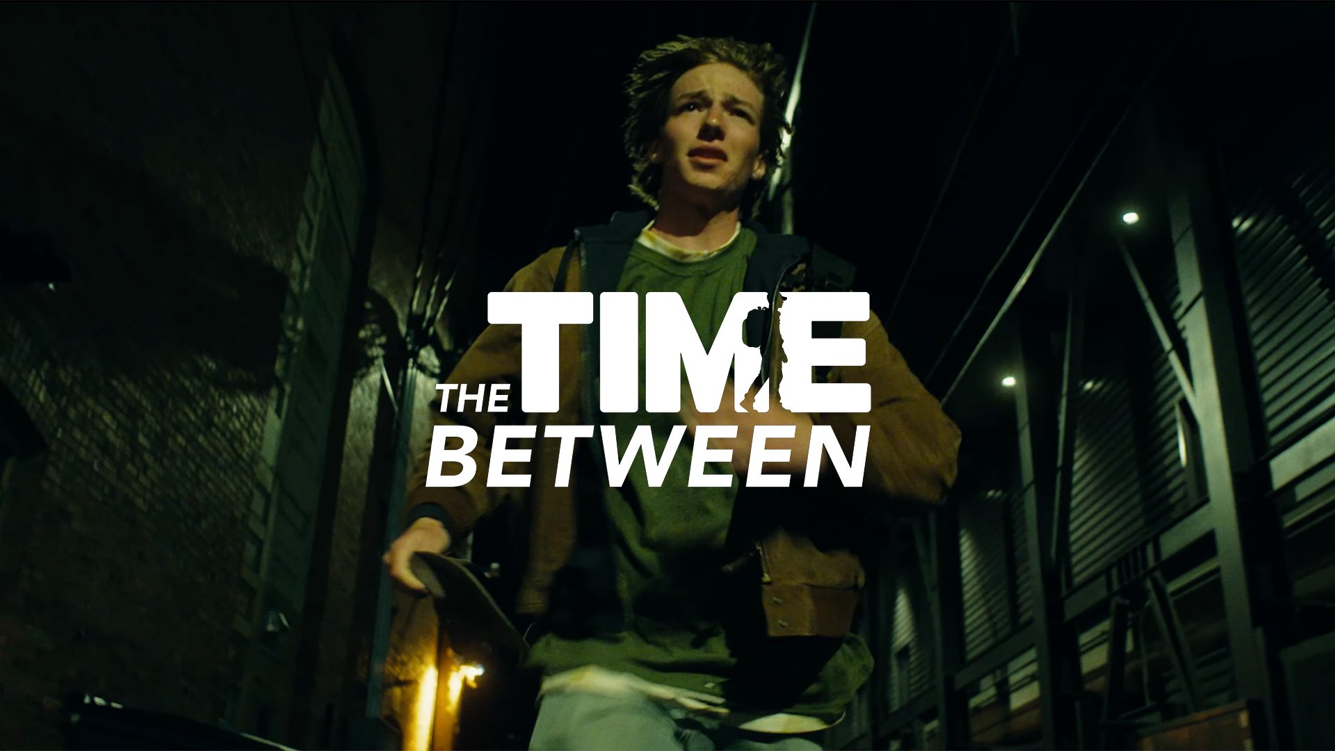 A young man running through a dark alley at night, holding a skateboard, with the text 'The Time Between' overlaid.