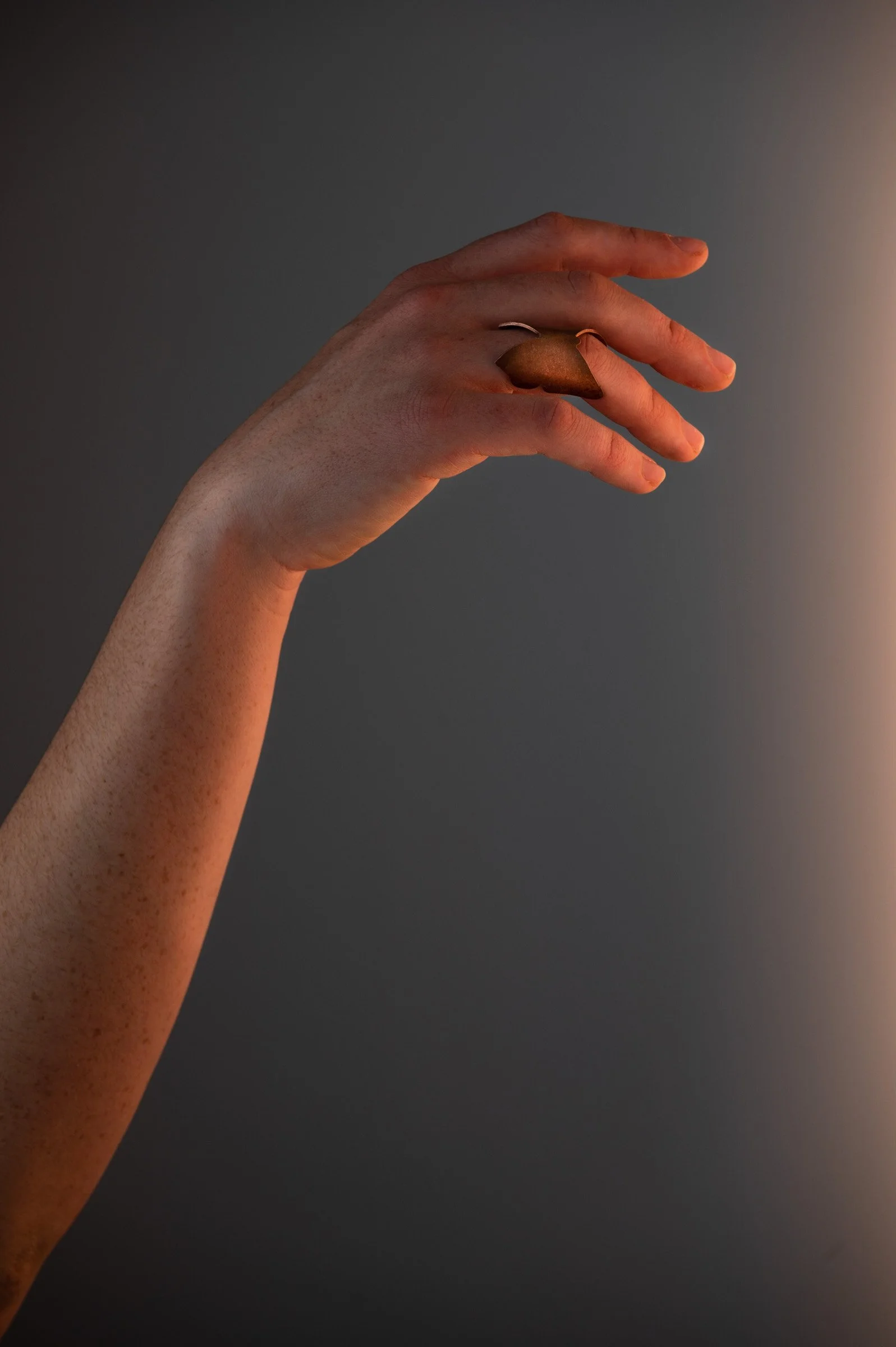 Close-up of a hand with a large brown ring on the finger against a dark gradient background.