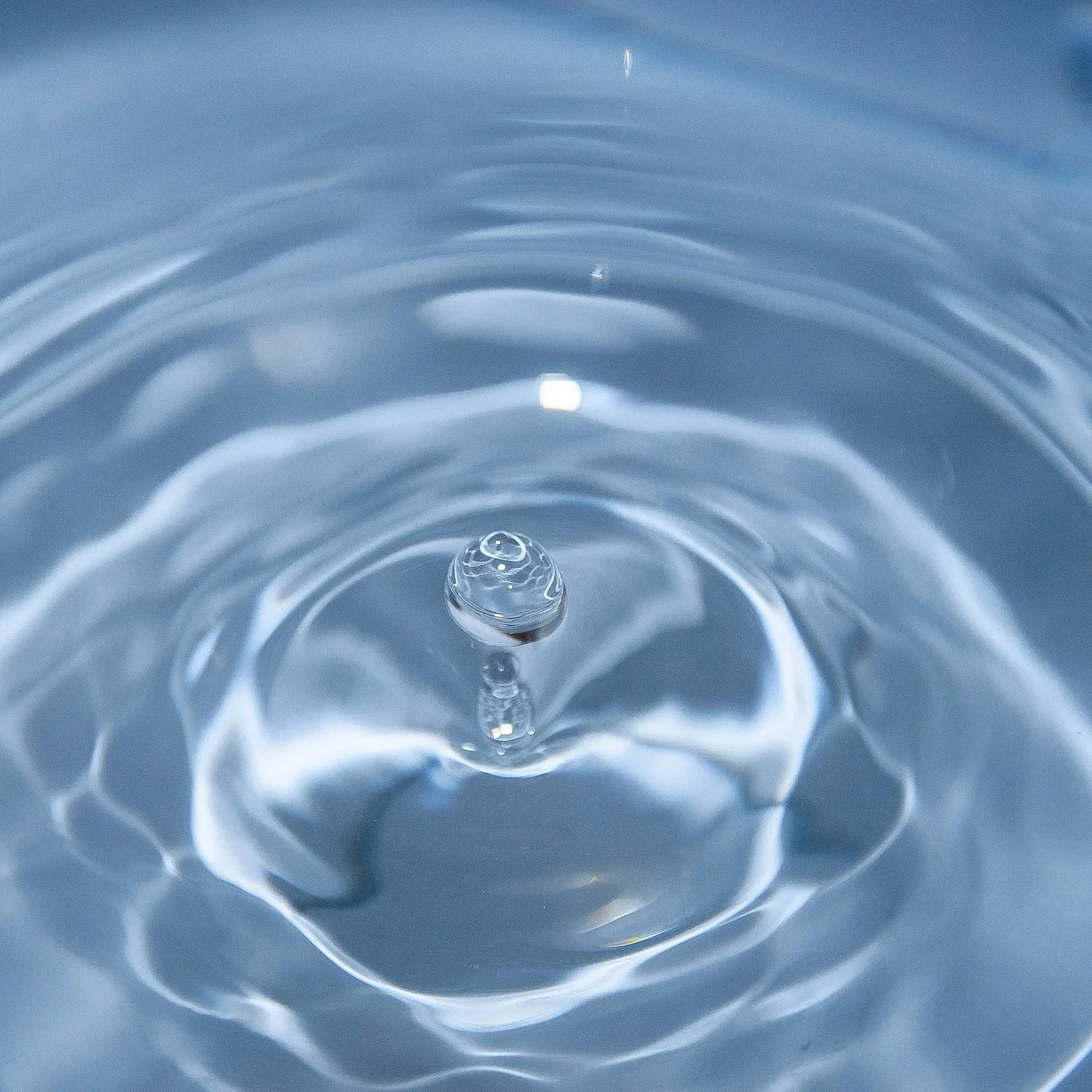 Close-up of a water droplet creating ripples on the water's surface. Representing cleansing.