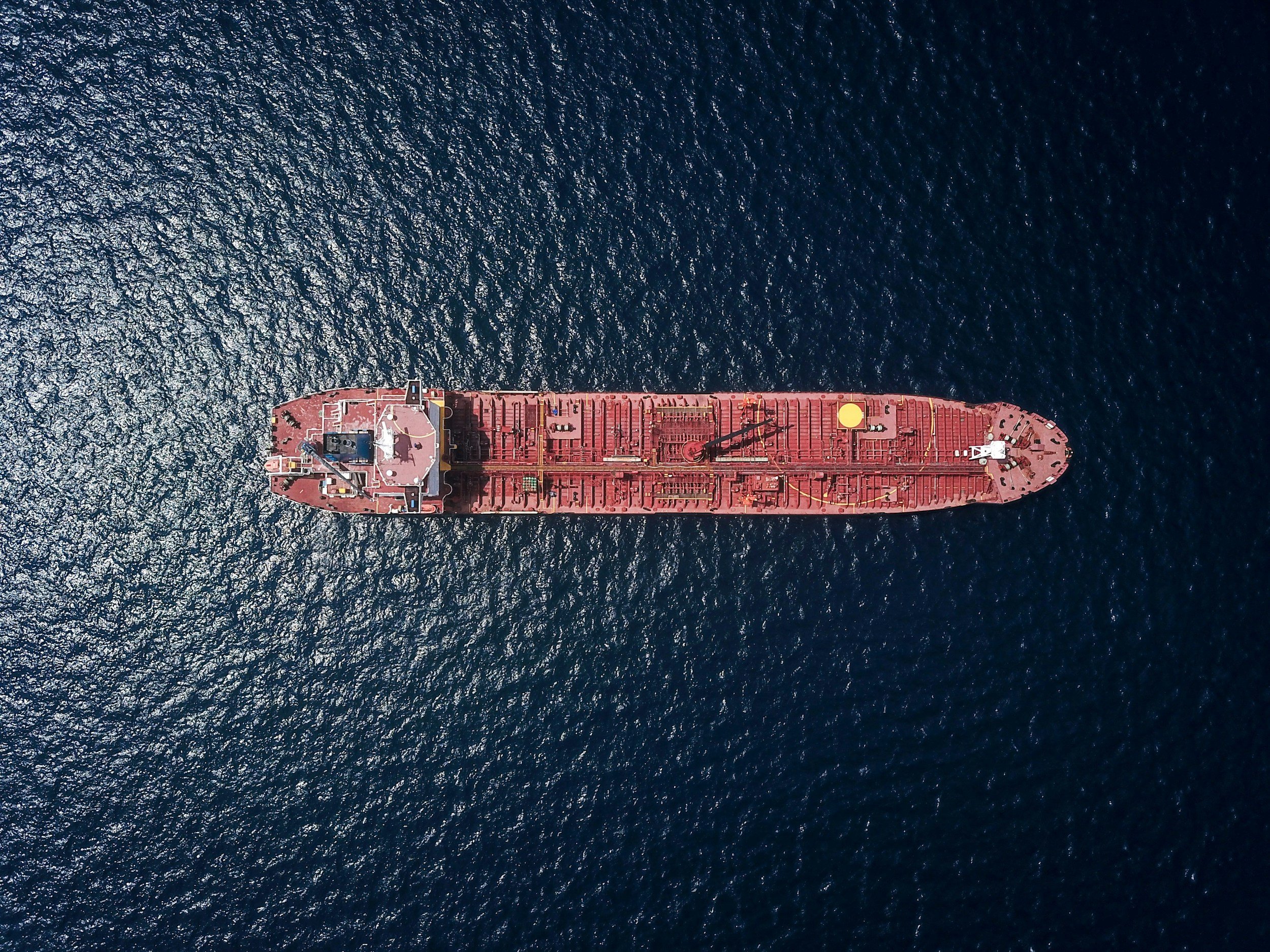Aerial view of a large red cargo ship sailing on the open ocean with gentle waves.