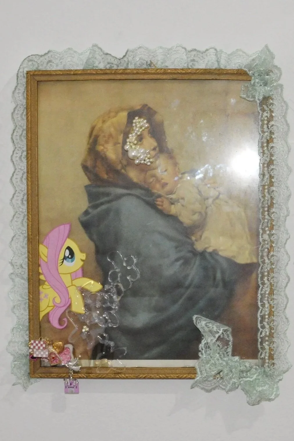 Framed artwork of an elderly woman holding a child, decorated with lace, pearl stickers, and cartoon character stickers.