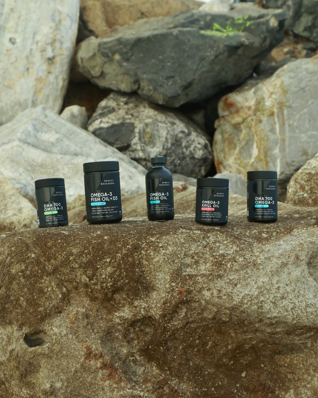 five black bottles of fish oil supplements with labels, placed on a large rock with a background of various-sized rocks and boulders.