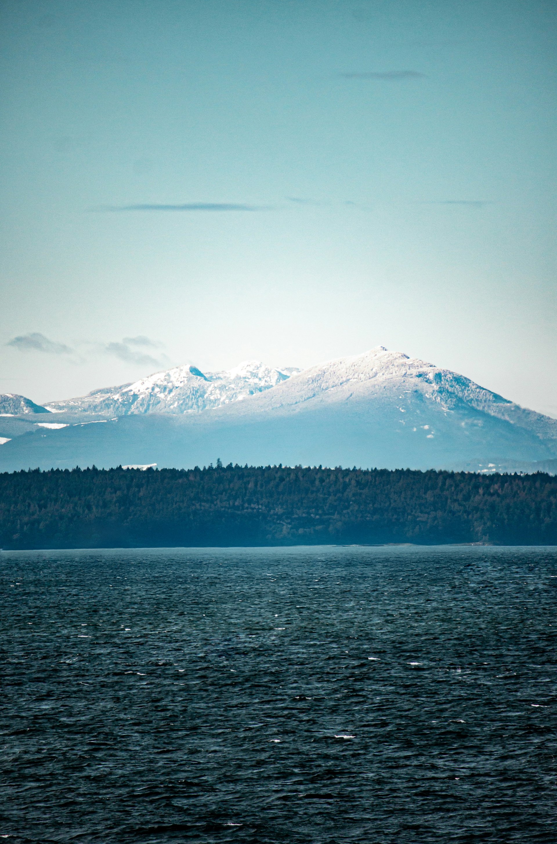 View of a lake with dark water and snow-capped mountains in the background under a clear sky.