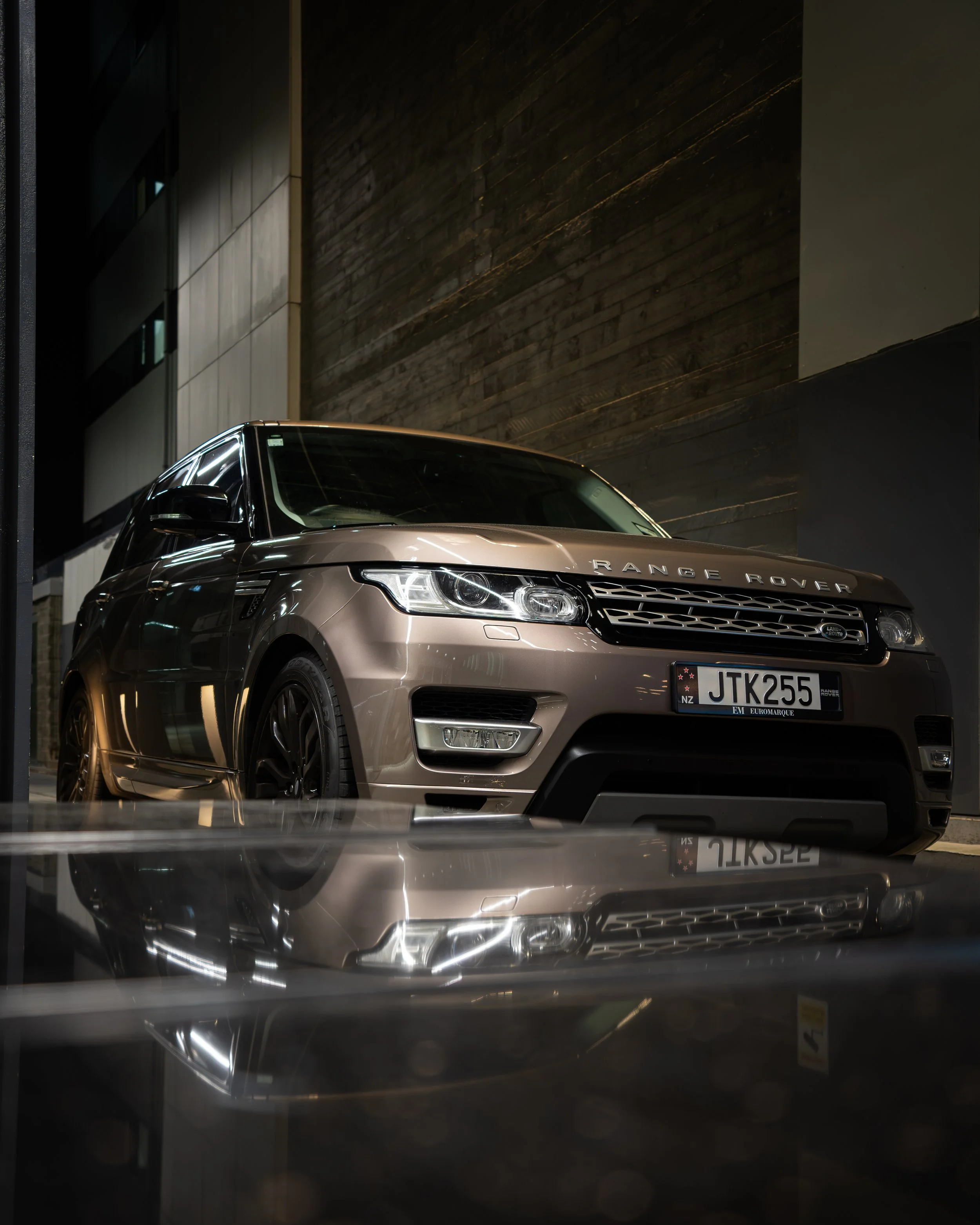 A luxury beige Range Rover SUV parked indoors at night with its reflection visible on the shiny surface below.