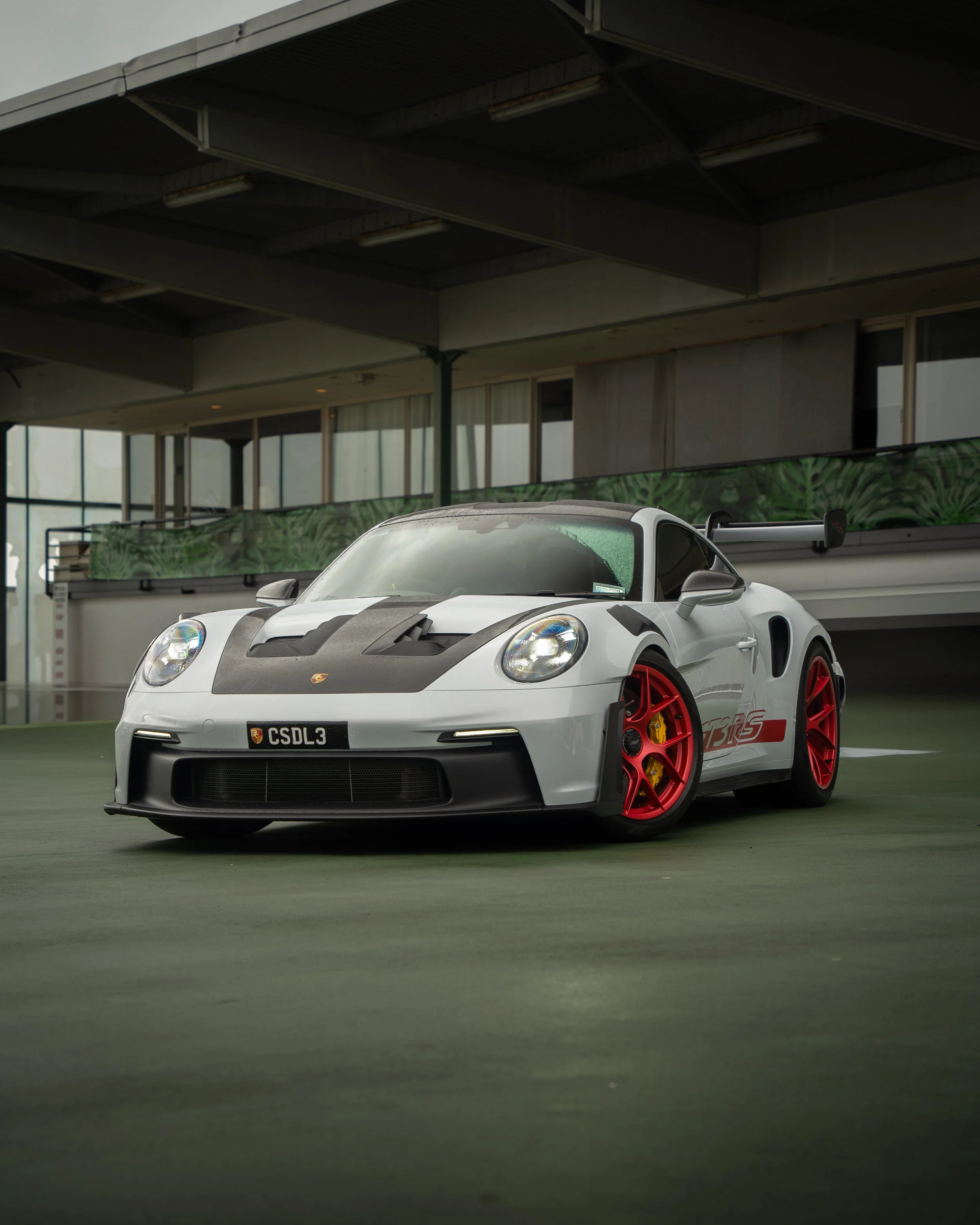 A white Porsche 911 GT3 RS with black hood and red wheels parked in an indoor garage.