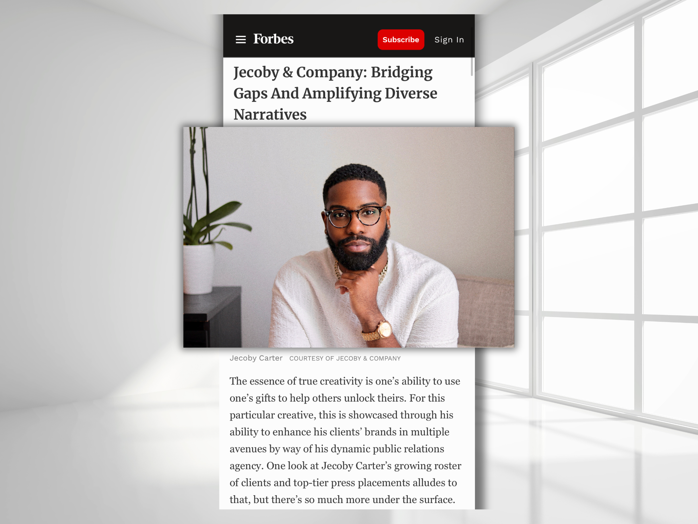 Photograph of a man with glasses, a beard, and gold jewelry, sitting indoors with a neutral background and a plant nearby, overlaid on a screenshot of a Forbes article.