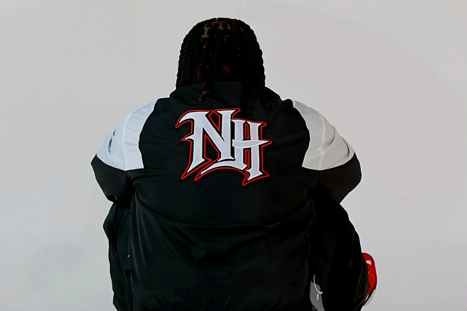 Back of a person wearing a black jacket with white shoulder panels and a bold red, white, and black logo on the back, standing against a plain gray background.