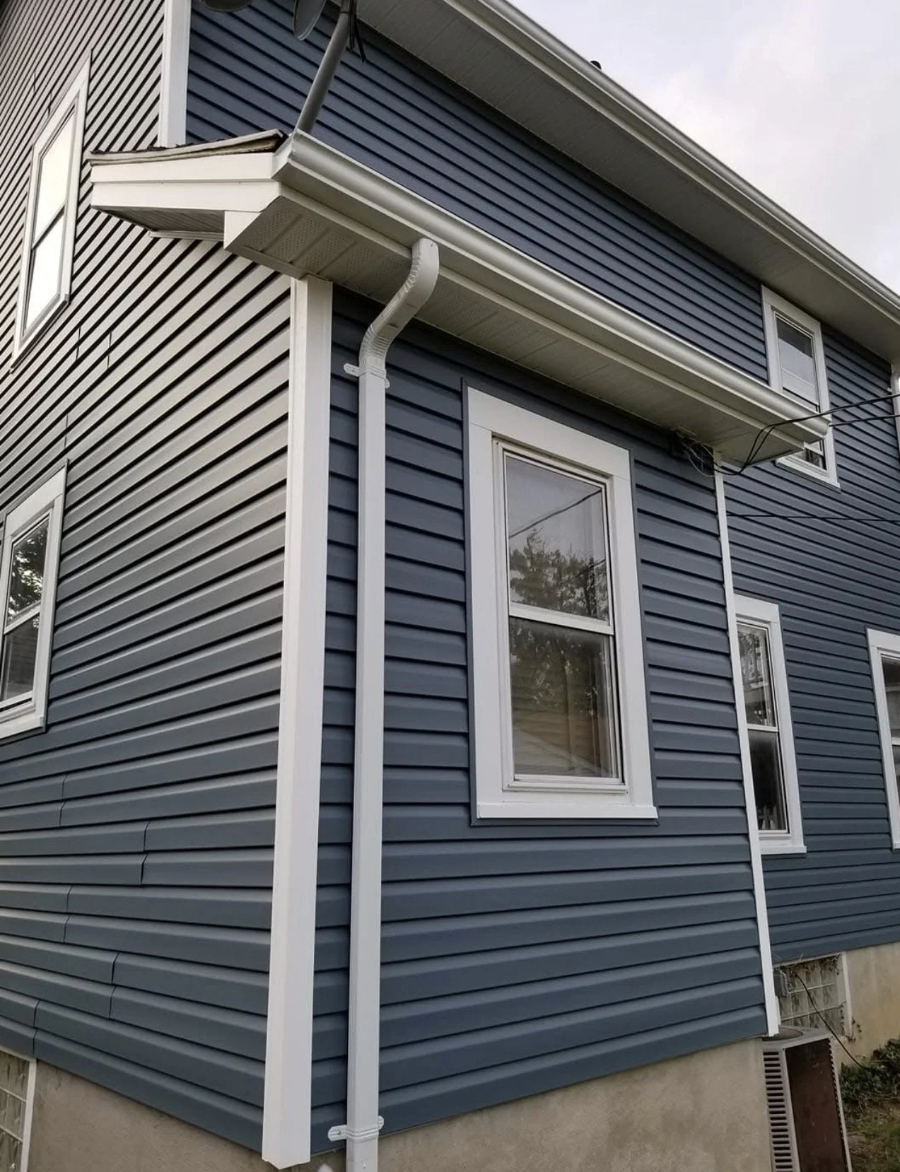Close-up of the blue house exterior with white-framed windows and white downspout.