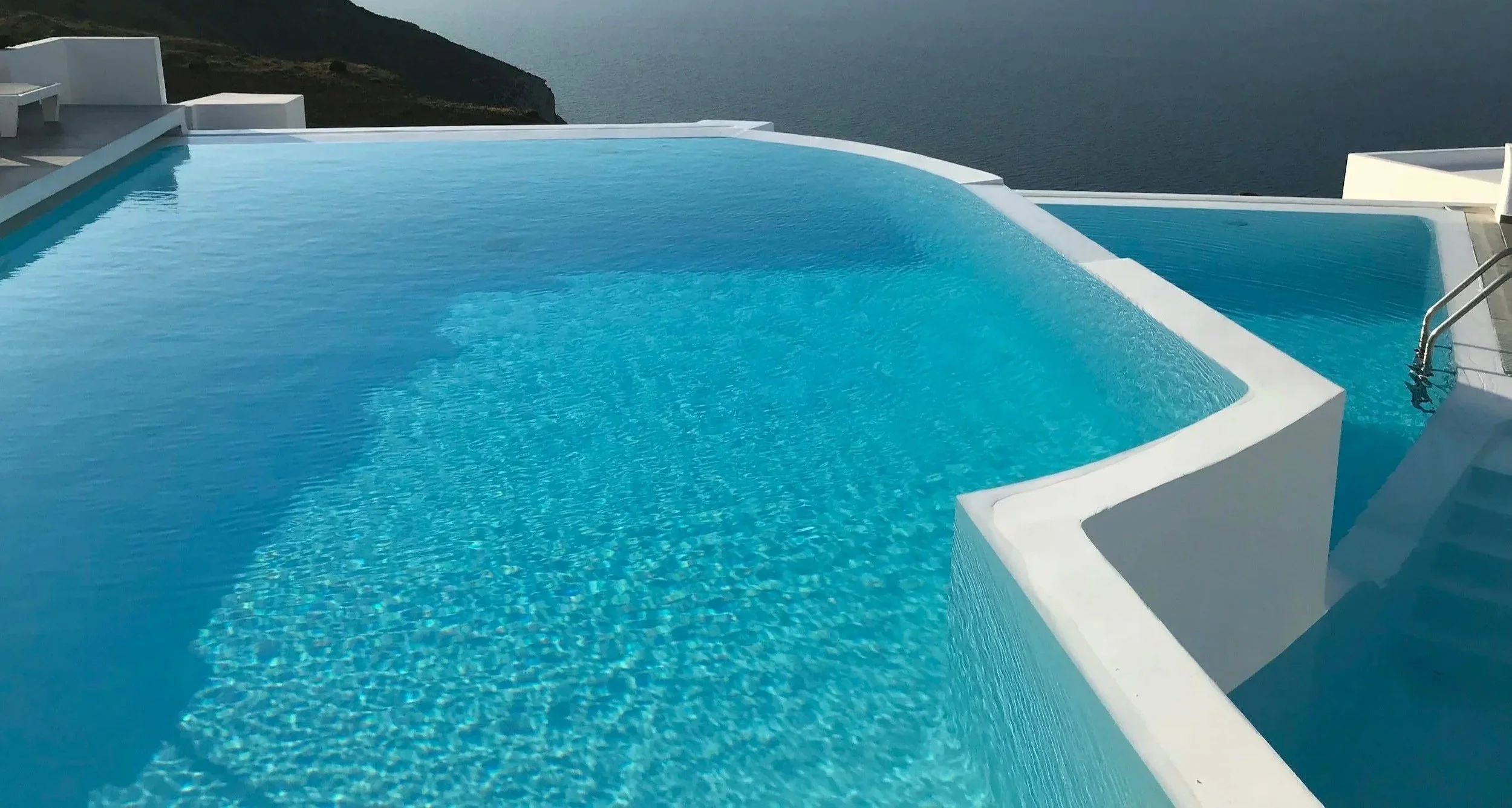 Infinity pool overlooking a body of water and mountains in the distance.
