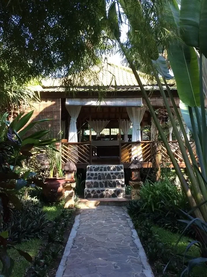 Pathway leading to a cozy wooden house with a stone staircase, surrounded by lush green tropical plants and trees.