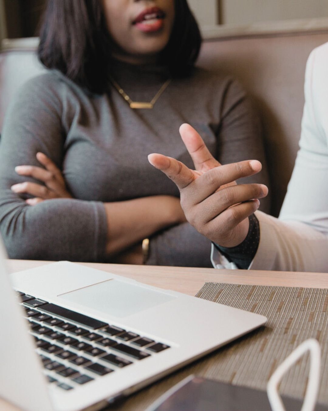 womans hand pointing at laptop screen with black woman sitting next to her arms crossed and listening to review