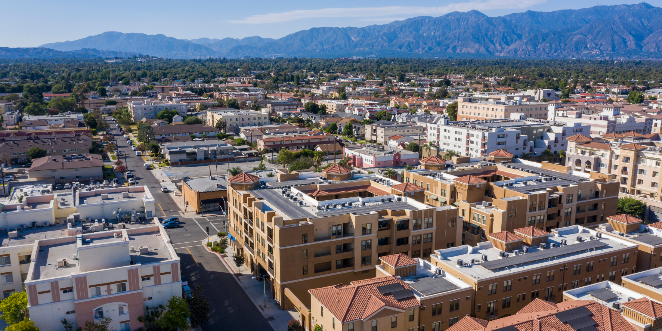 Aerial view of a city with multiple mid-rise and low-rise residential and commercial buildings, with mountains in the background.