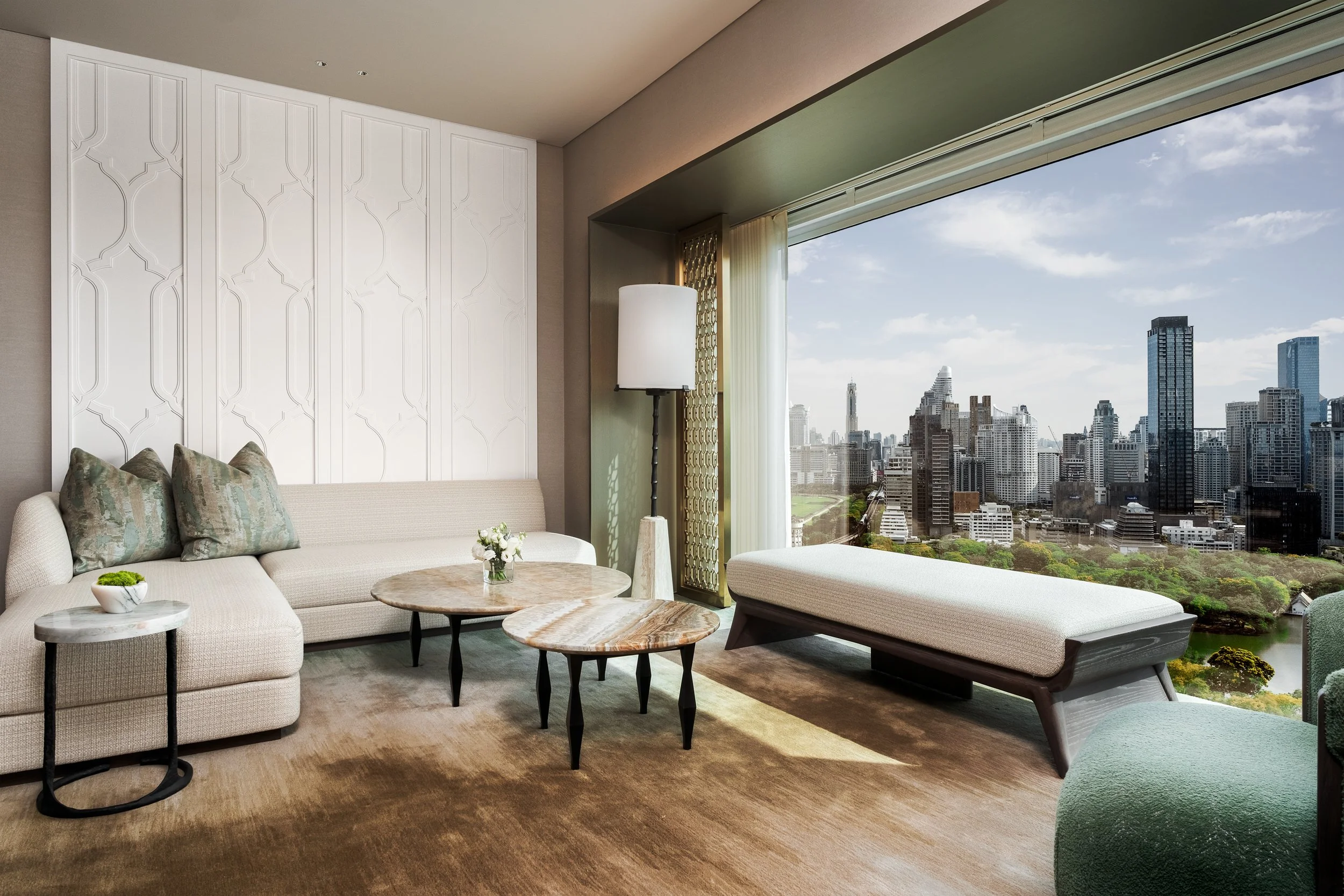 Upscale Living room with a beige sectional designer sofa, three marble-top coffee tables, a floor lamp, a large window showing Bangkok's city skyline view, and a green accent chair.