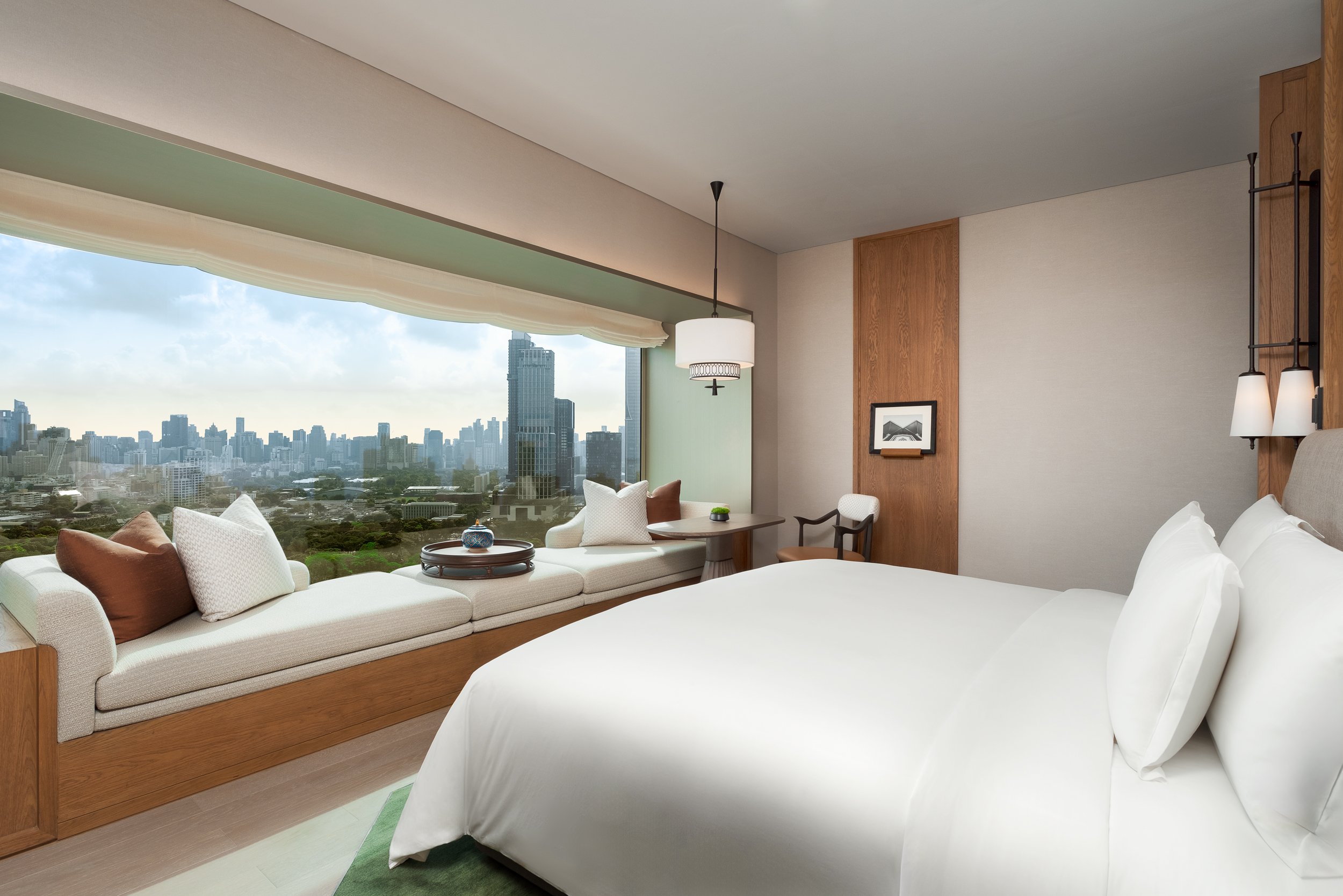Luxury hotel room with a panoramic window showing Bangkok skyline & Lumpini Park. 