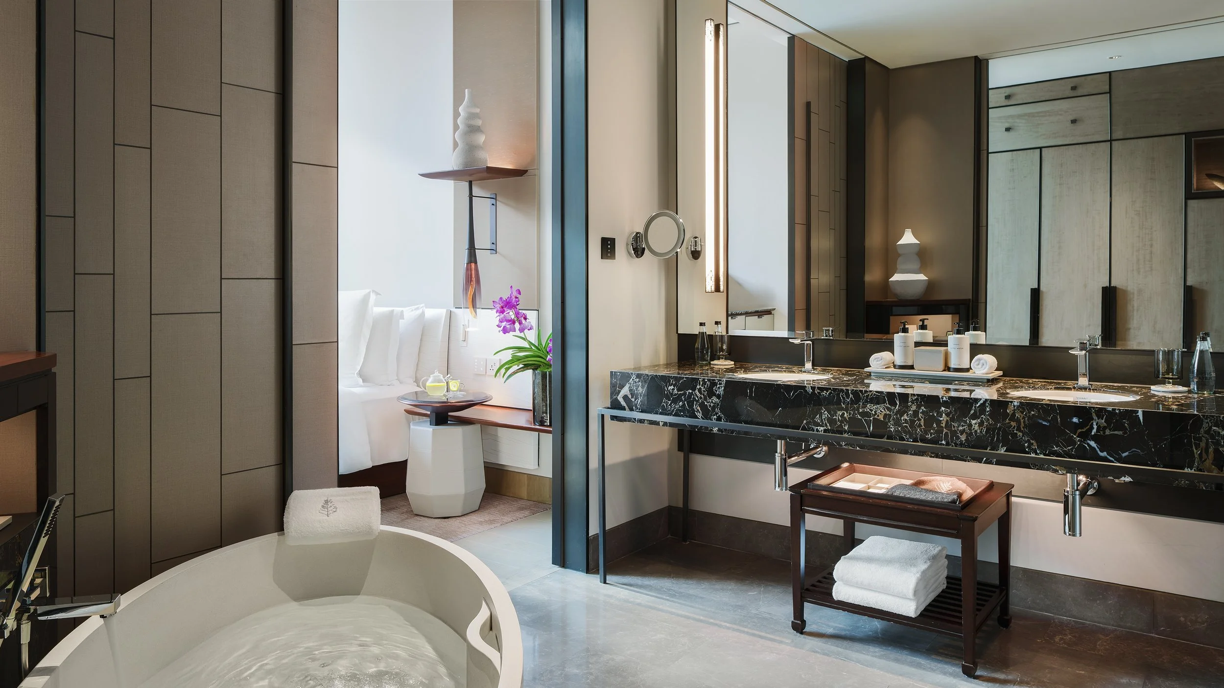 Luxury hotel bathroom with black marble double sink vanity, large mirror, soaking tub, luxury designer amenities, decorative vases and flowers in a luxury resort in the wide Asia region.