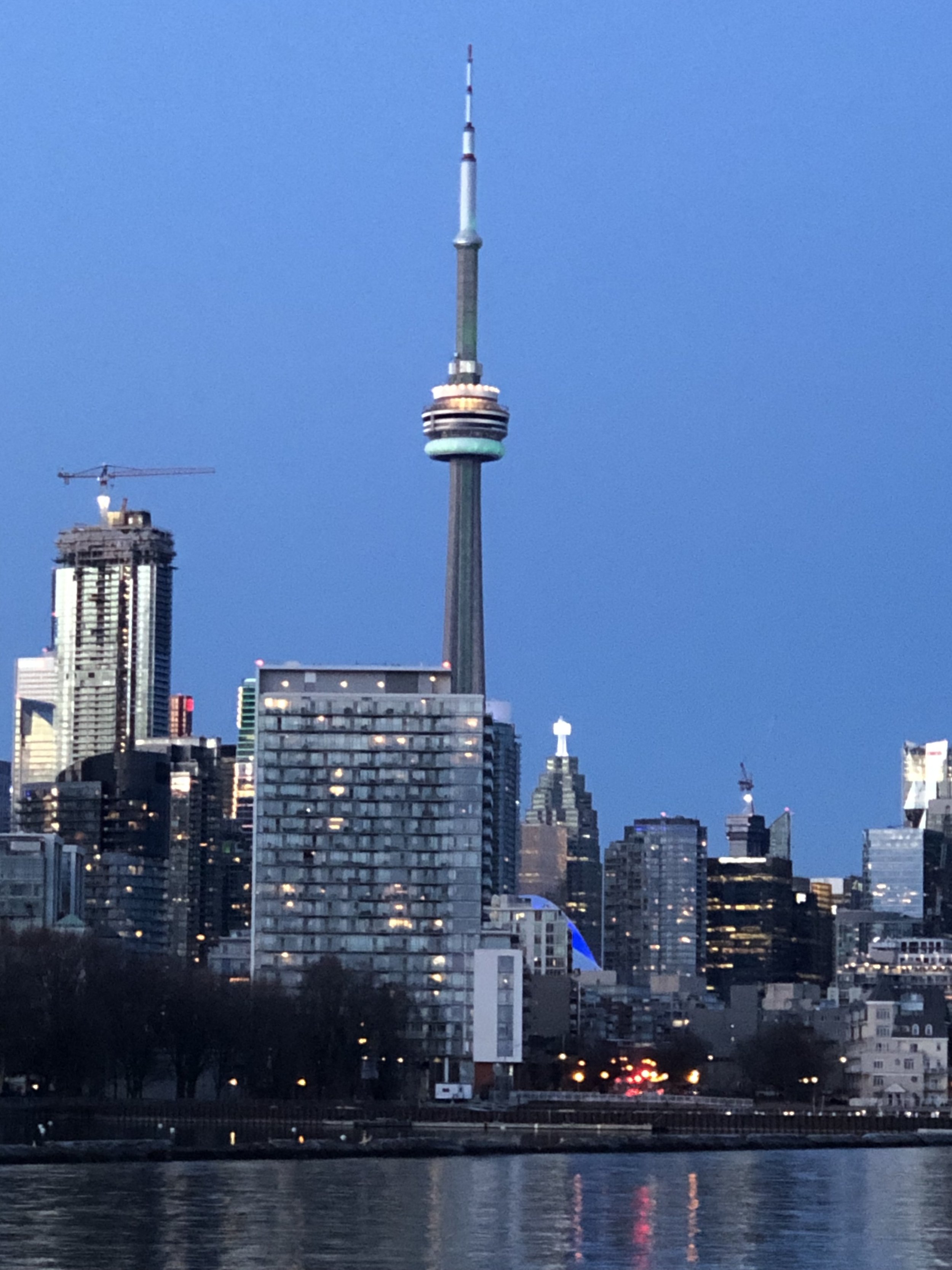 Night view of Toronto skyline featuring the CN Tower illuminated, with buildings and the sky reflecting in the water in the foreground.