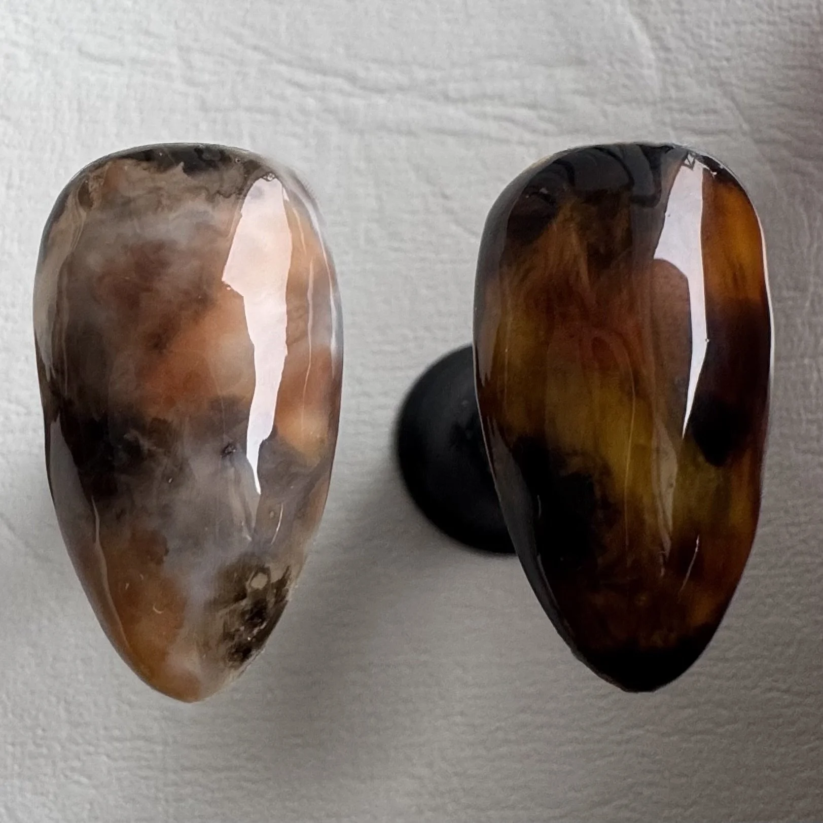 Close-up of two tortoiseshell press-on nails, one light and the other dark brown, placed on a white surface.