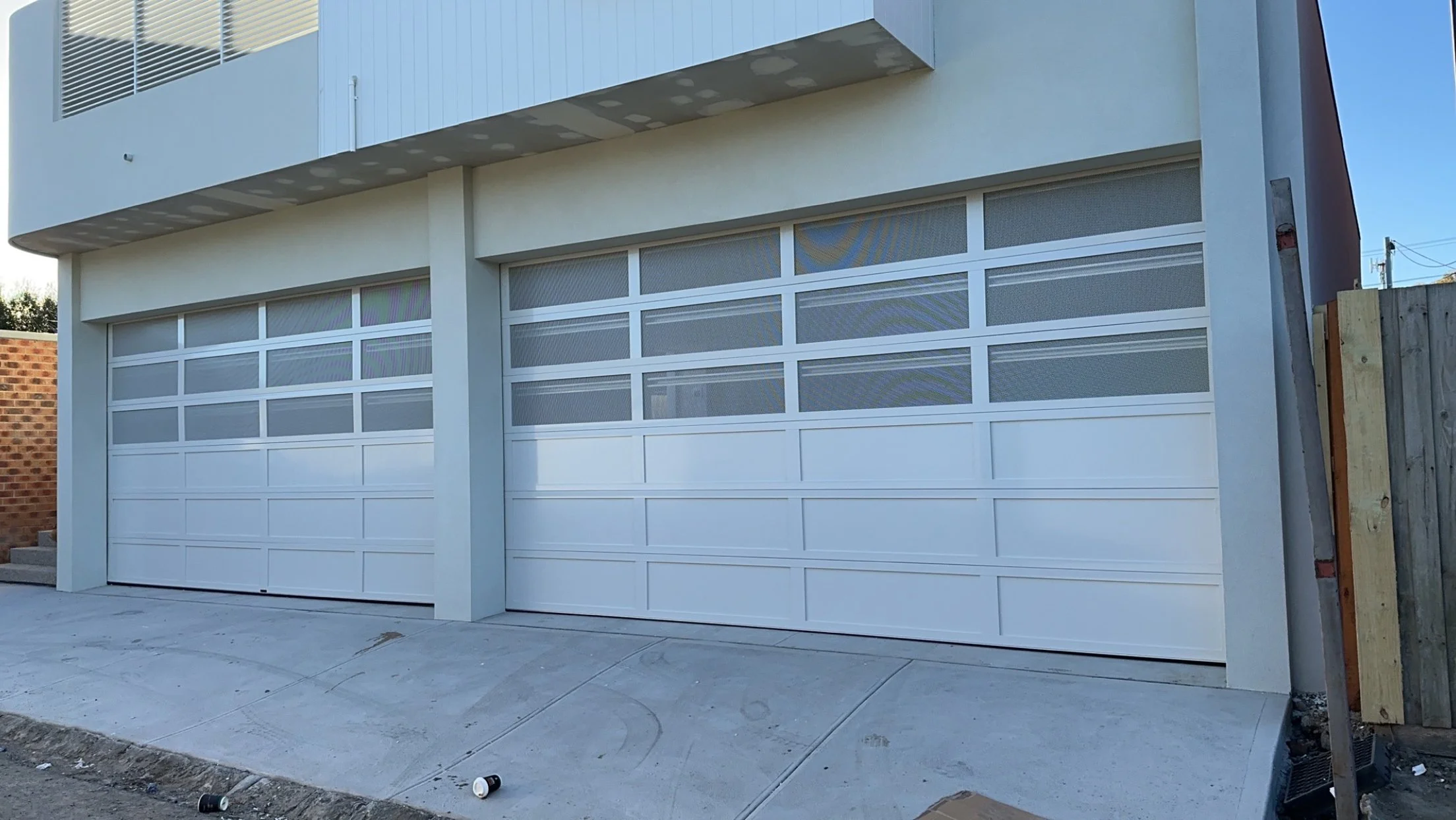 Two white modern garage doors with glass panels on a new building
