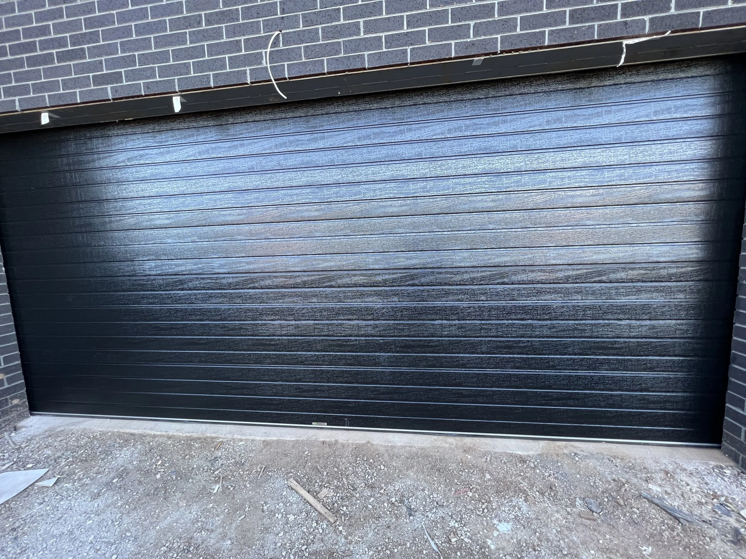 Black garage door with horizontal panels, installed in a brick wall