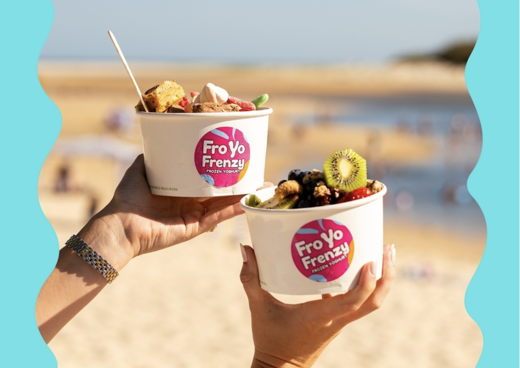 Two hands holding cups of frozen yogurt with the logo 'FroYo Frenzy' against a beach background. The cups are topped with various fruits and toppings.