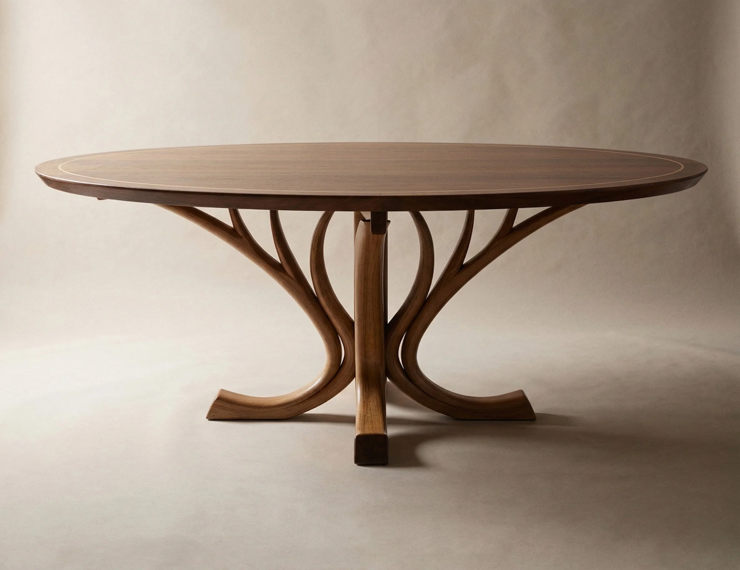 Round wooden dining table with a hand-sculpted curved trestle base resembling elegant branches and a smooth, oval top against a plain minimalist background. Handmade in Brisbane Australia from Tasmanian Blackwood by Furniture Maker, Will Marx