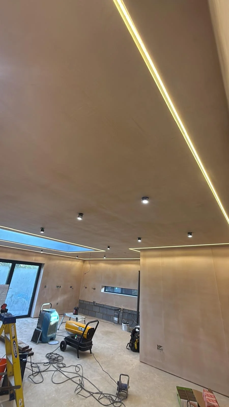 Room under construction with unfinished floors, tools, and light fixtures on the ceiling.