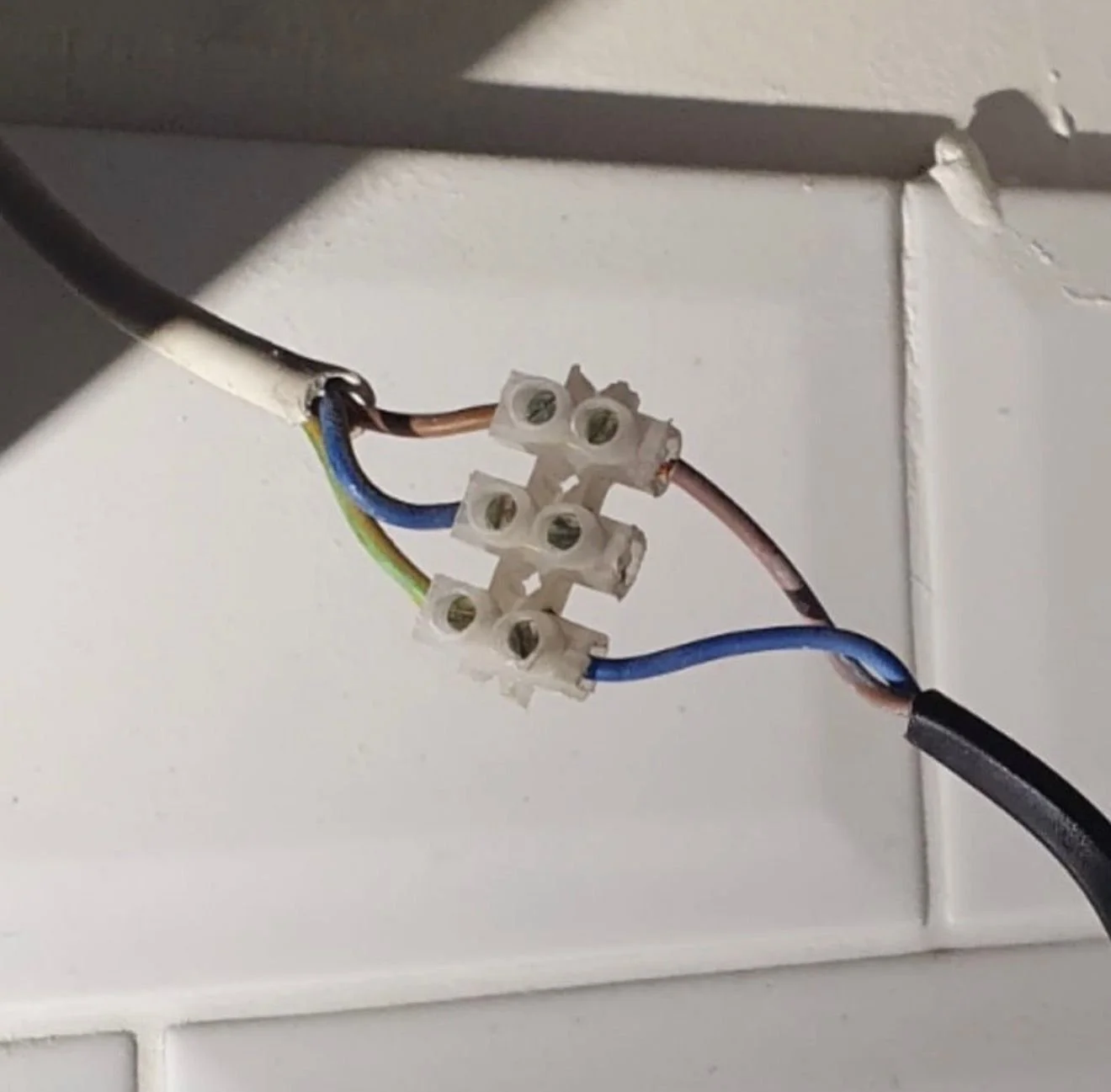 Close-up of an electrical wire connector with three wires, attached to a white wall or outlet box.