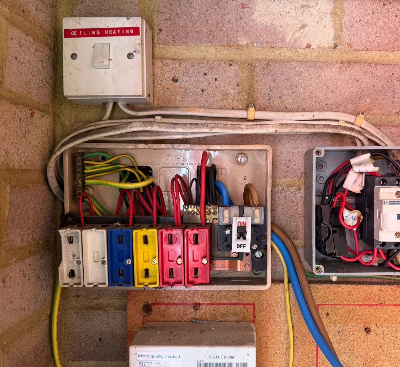Open electrical panel with circuit breakers and wiring, mounted on a brick wall, labeled for ceiling heating.