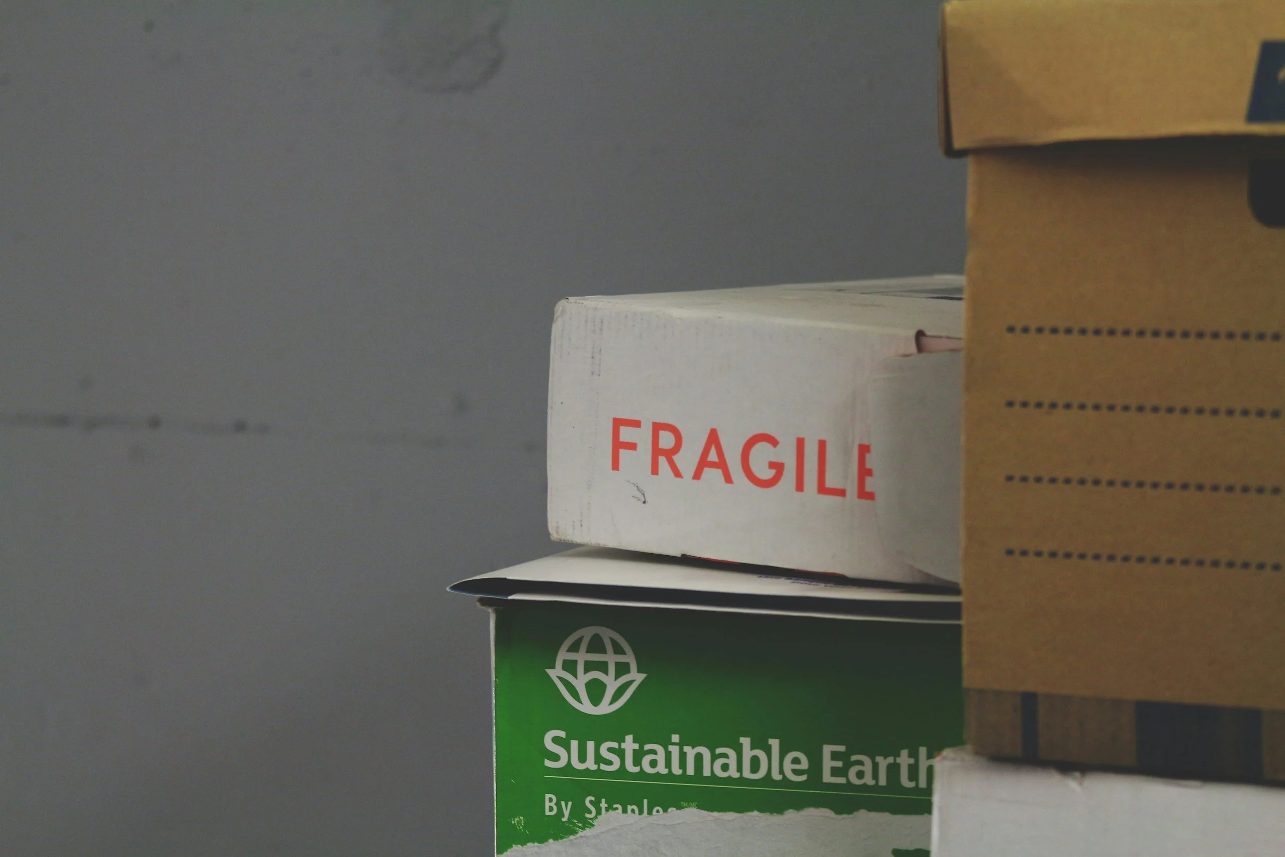 Primo piano di una pila di scatole di cartone, una con l'etichetta "Fragile" e un'altra con l'etichetta "Terra Sostenibile" e il logo di un globo terrestre