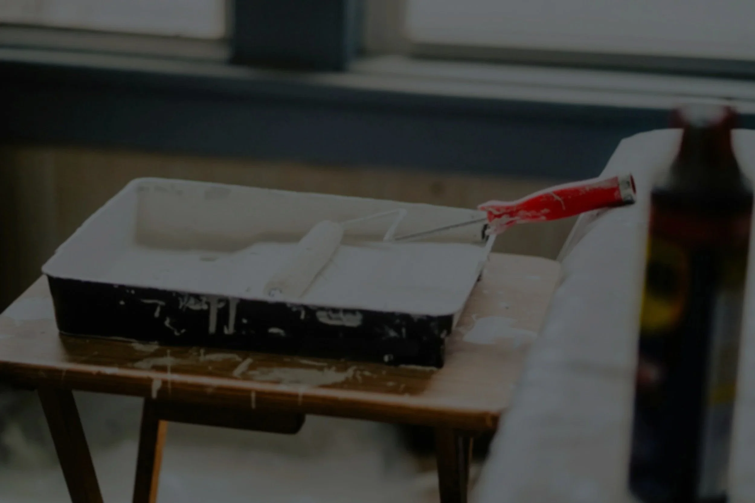 Rullo per pittura immerso in vernice bianca, dentro una contenitore di plastica appoggiato sopra ad un tavolo da lavoro di legno