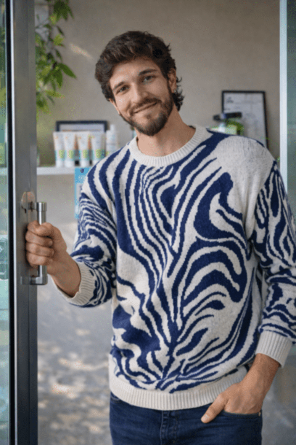 Santiago Jaramillo-Angel smiling in a striped sweater, holding open a glass door