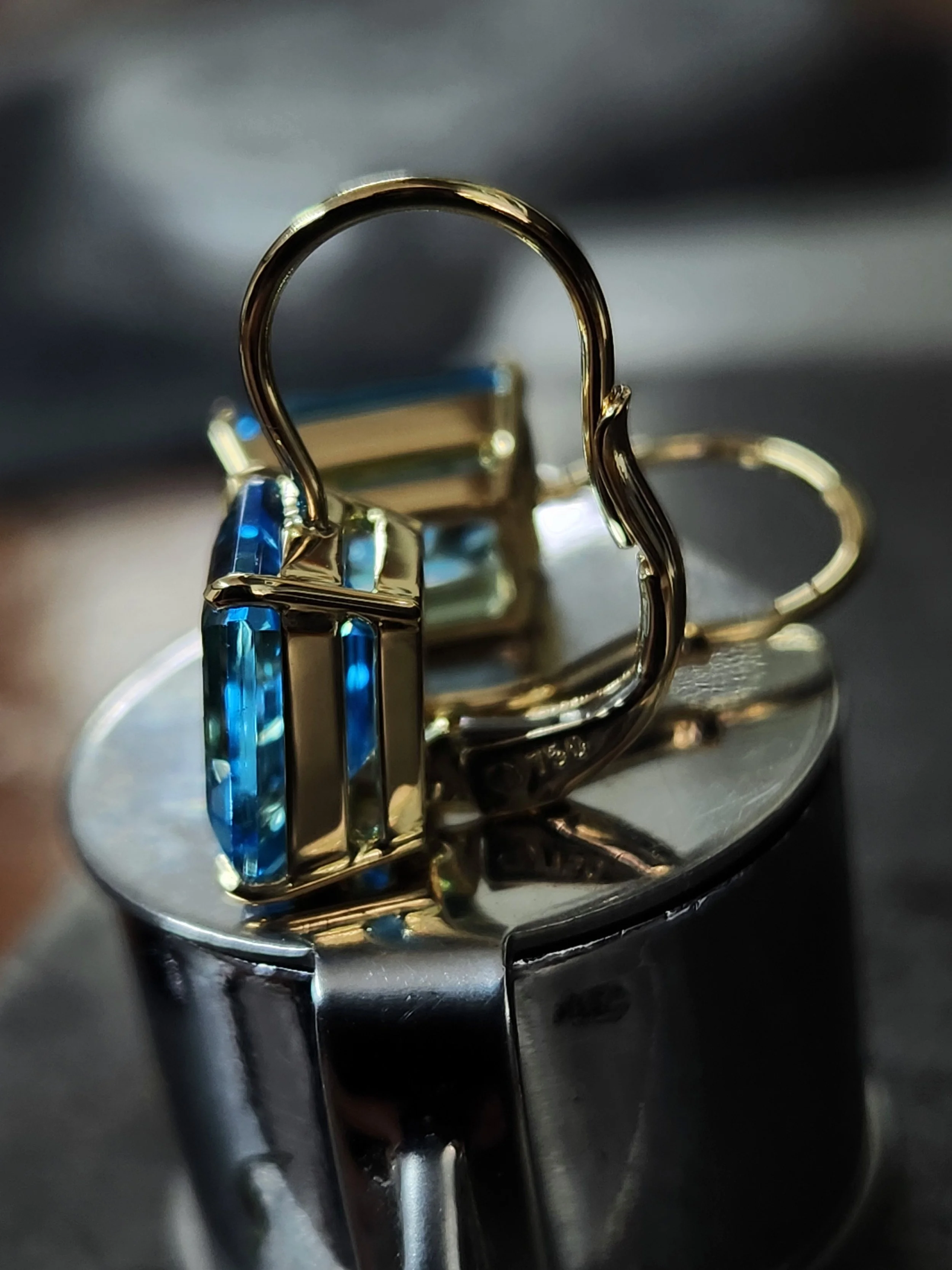 Close-up of a yellow gold pair of earrings with two swiss blue topaz gemstones with a continental  clip.