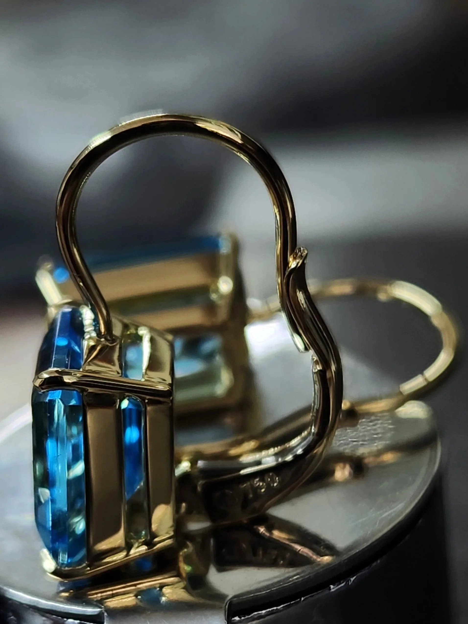 Close-up of a yellow gold pair of earrings with two swiss blue topaz gemstones with a continental  clip.