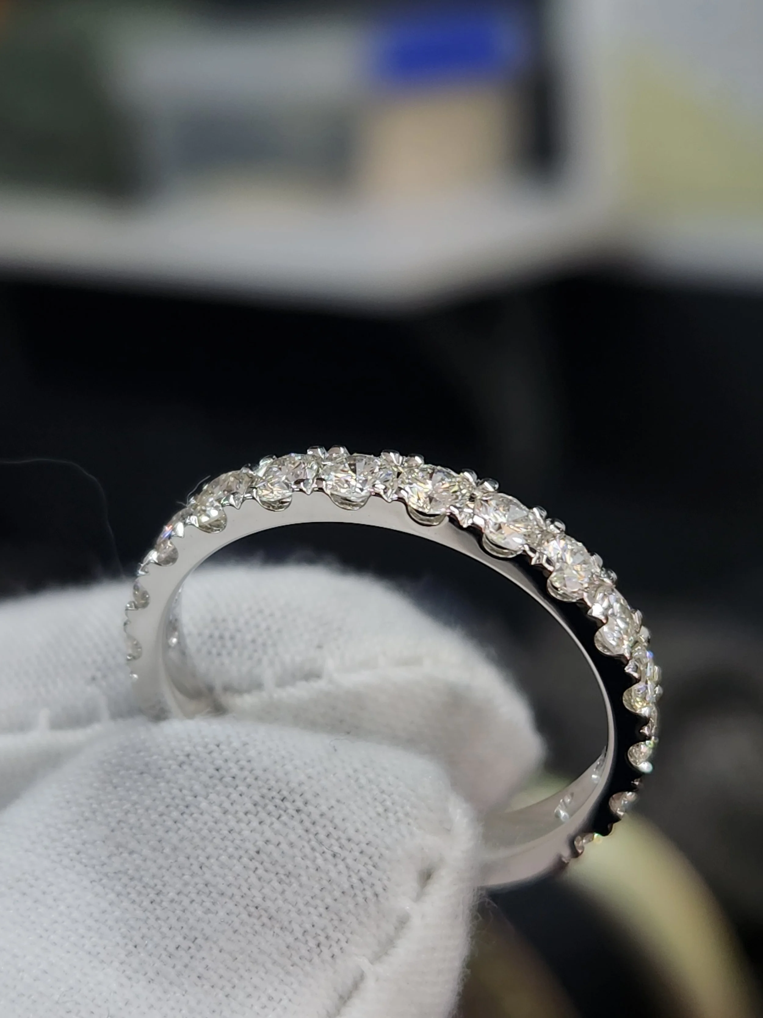 A handmade white gold wedding ring adorned with small round brilliant cut near-colourless natural diamonds, held by a hand wearing a white glove.