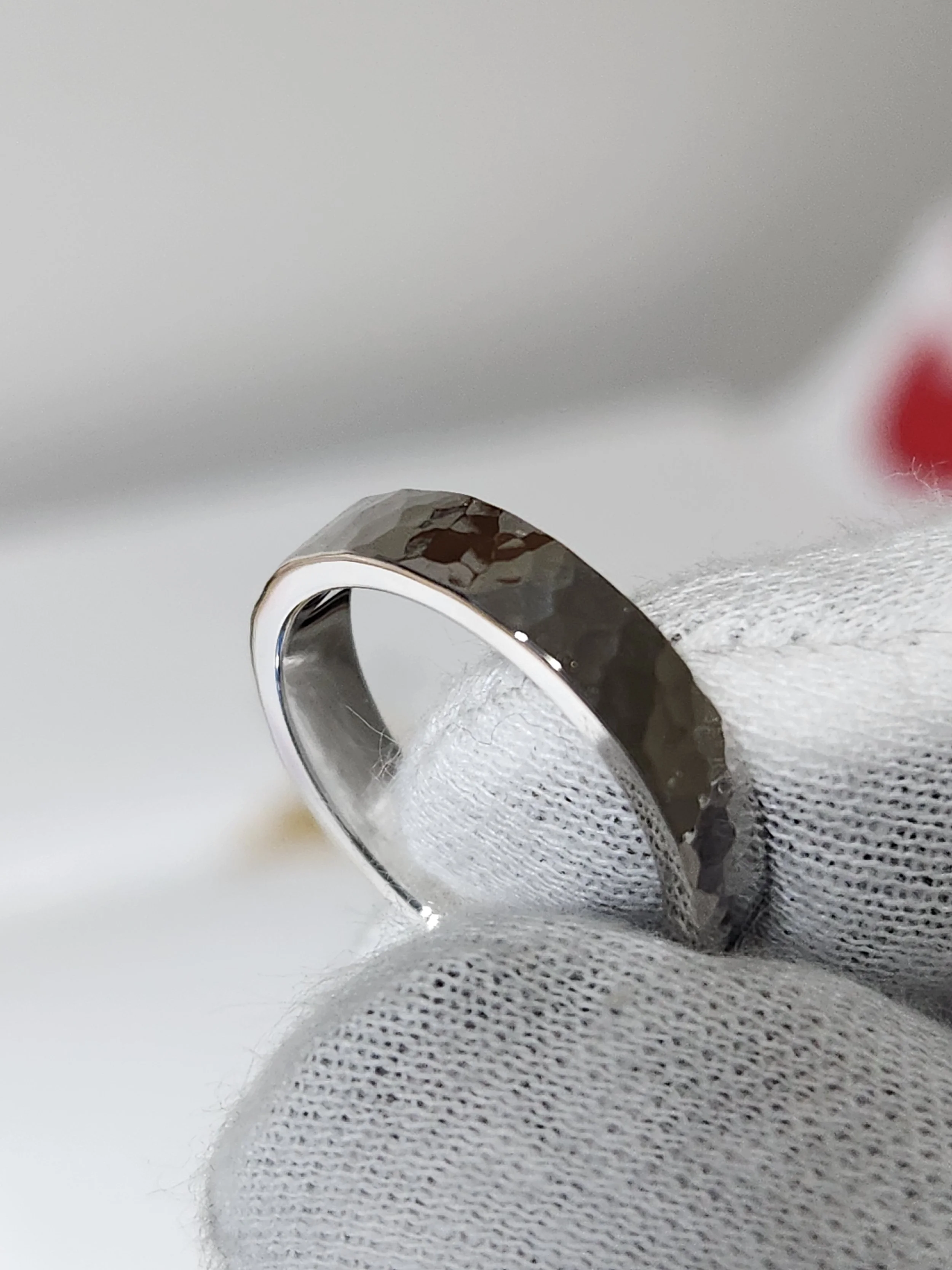 Close-up of a silver ring with a hammered texture, held by a white-gloved hand against a plain background.