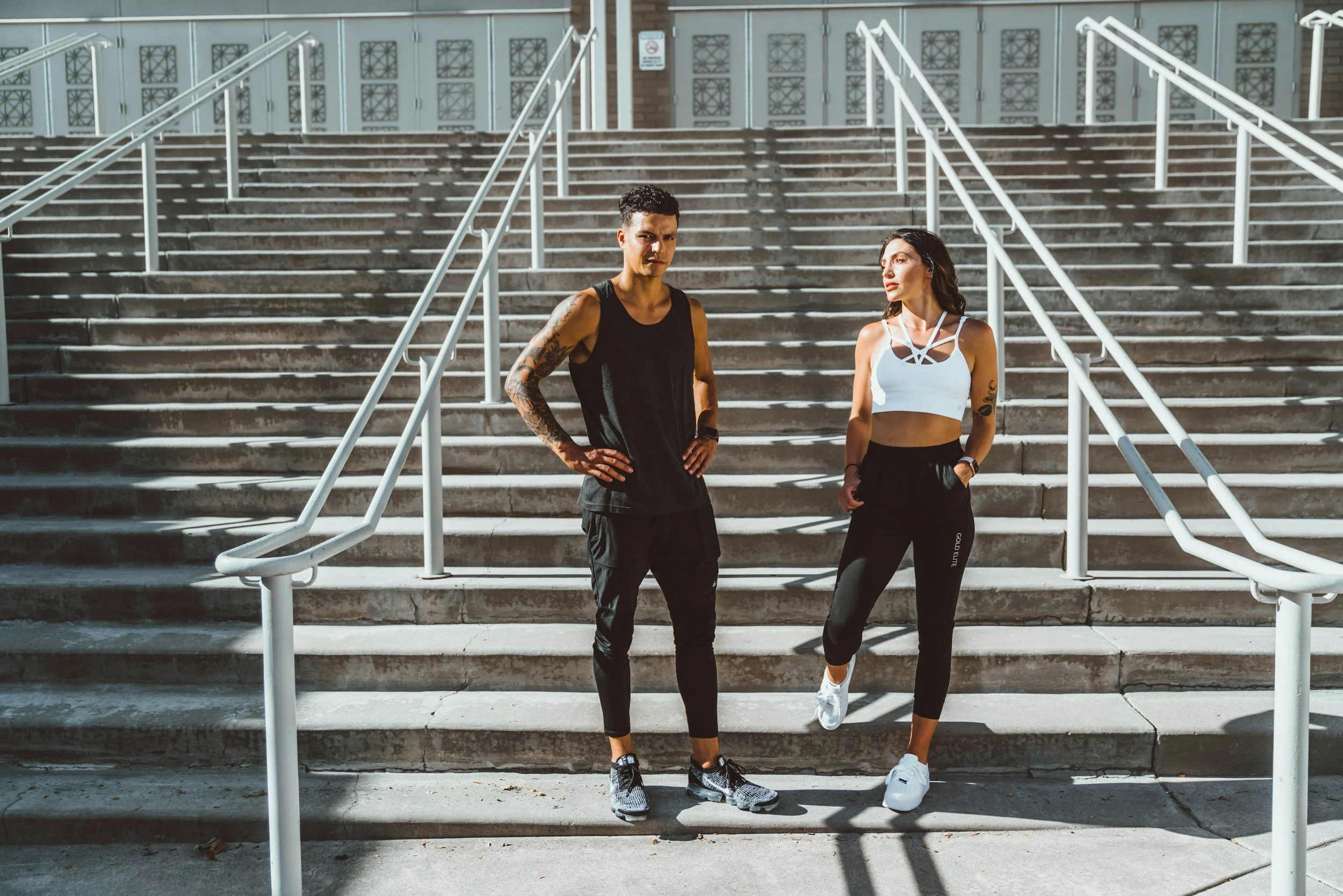 A man and woman in workout clothes standing on stairs outside, facing each other.
