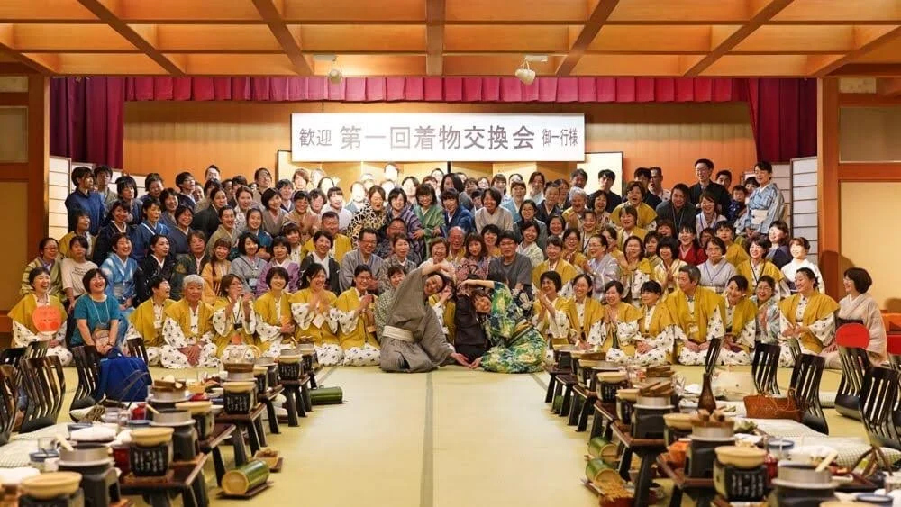 多くの人が着物を着て座り、背後に看板がある宴会の写真