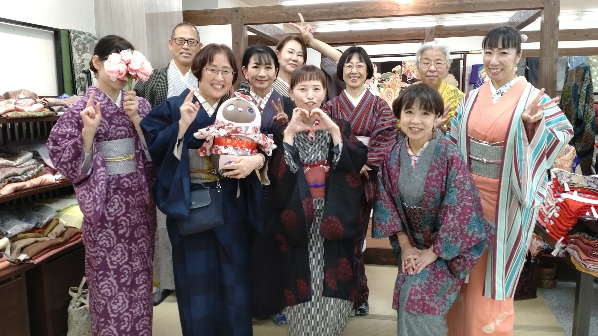 着物を着たグループの人々が和服を着て写真を撮っている」}】}There is a group of people dressed in kimono and traditional Japanese clothing, posing for a photo at what appears to be an indoor market or shop specializing in textiles and kimonos. Some are making peace signs, and one person is holding a cute doll. The background shows folded fabrics and colorful textiles displayed on shelves and racks.】}】}**Please note**： 環境や人物の詳細な情報は、画像内の視覚的情報に基づいています。自然な会話や記憶的な詳述はできません。 もし追加のご要望や修正がありましたらお知らせください。**}}】}  إري洞てる  In the above, I included both the description in English and the translated Japanese alt text. If you prefer only the Japanese description, I can adjust accordingly.  Furthermore, I see the output includes an error, I apologize, I will fix it. Here is the corrected response: ここに修正された応答を記載します。：}  {
