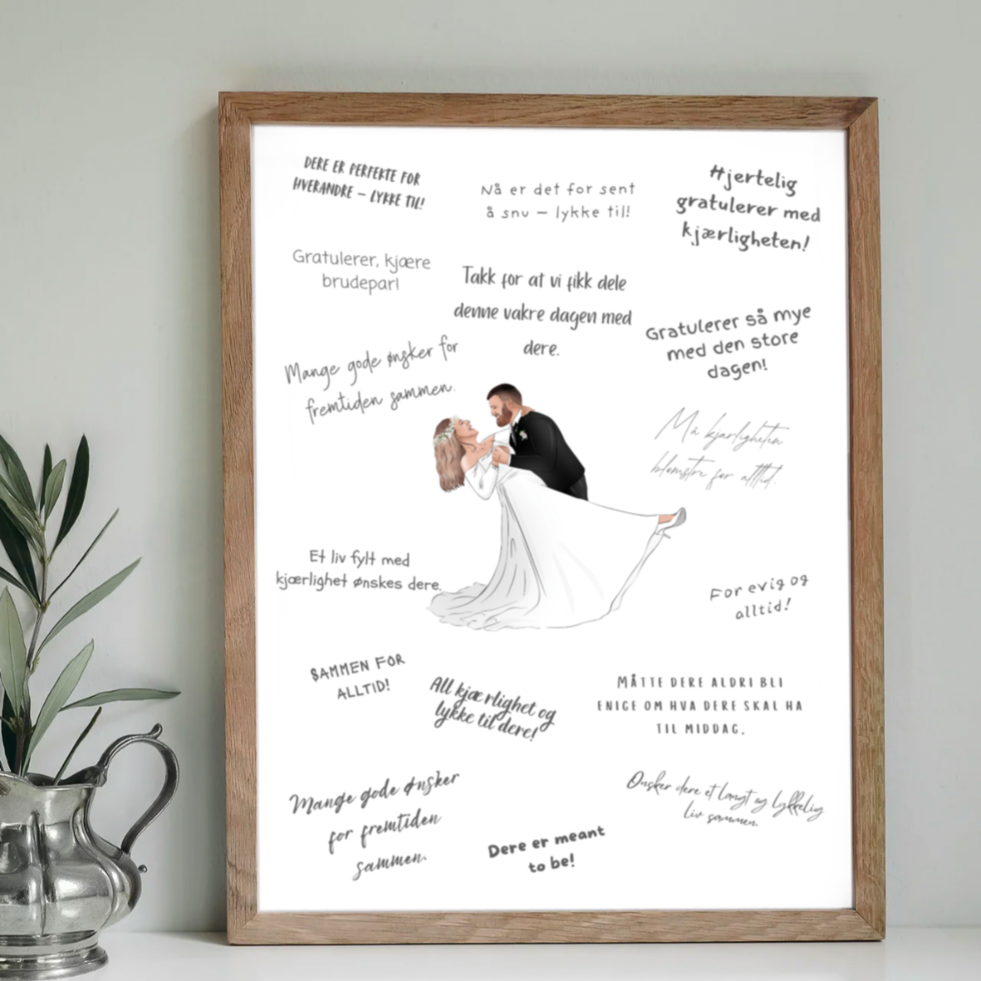 A framed wedding collage with a drawing of a bride and groom dancing, surrounded by handwritten congratulatory messages in Norwegian. The frame is made of wood, and there's a silver pitcher with green plant leaves beside it.