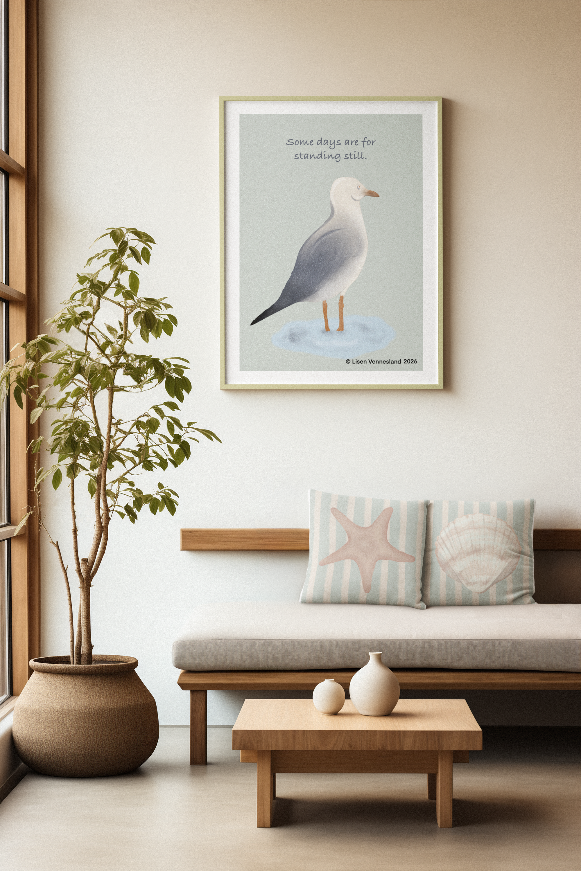 Living room with a framed art print of a bird on the wall that reads "Some days are for standing still." A sofa with striped pillows featuring a starfish and a shell, a wooden coffee table with vases, a large potted plant, and a window with natural l