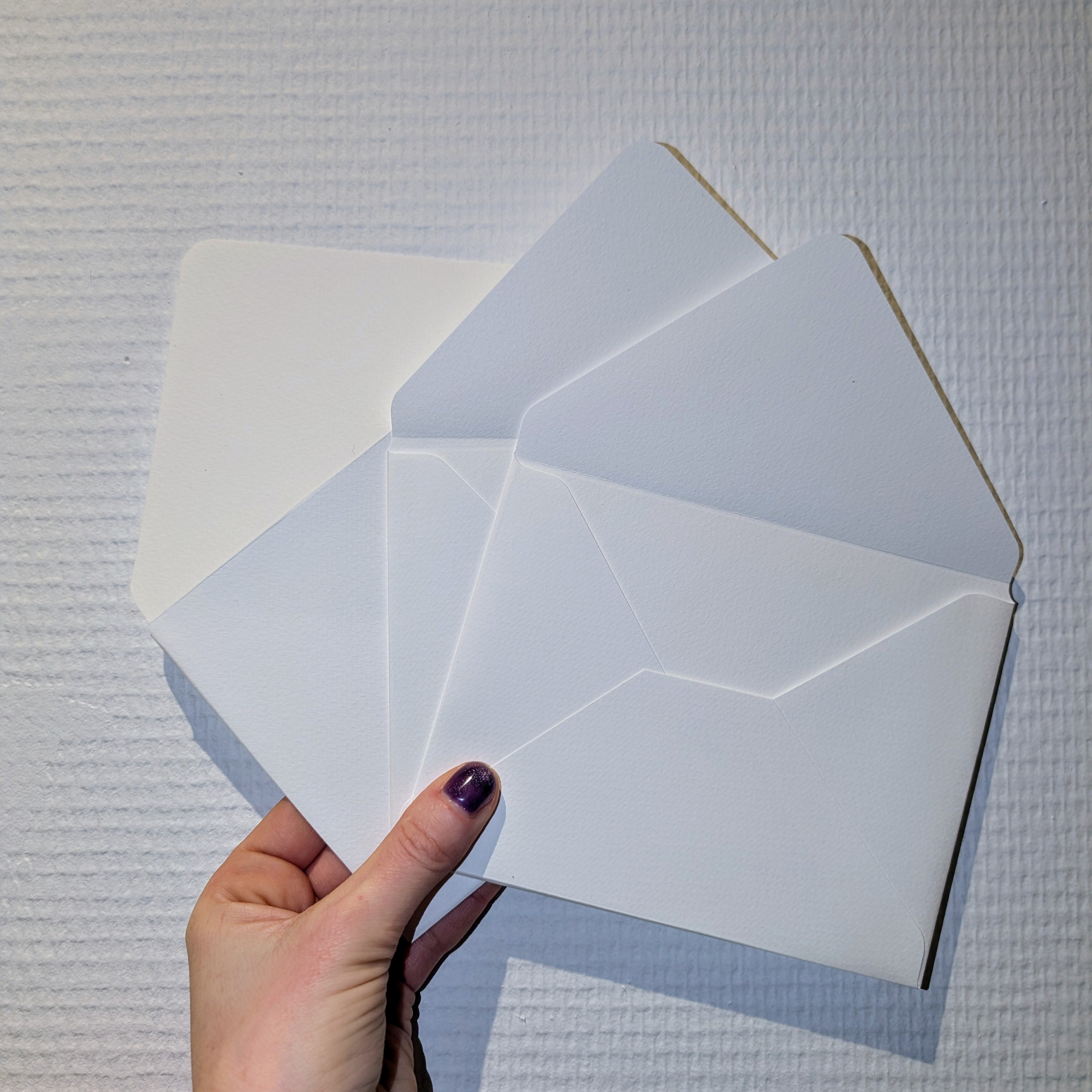 A hand holding a white paper open, revealing blank pages, against a textured white wall background.