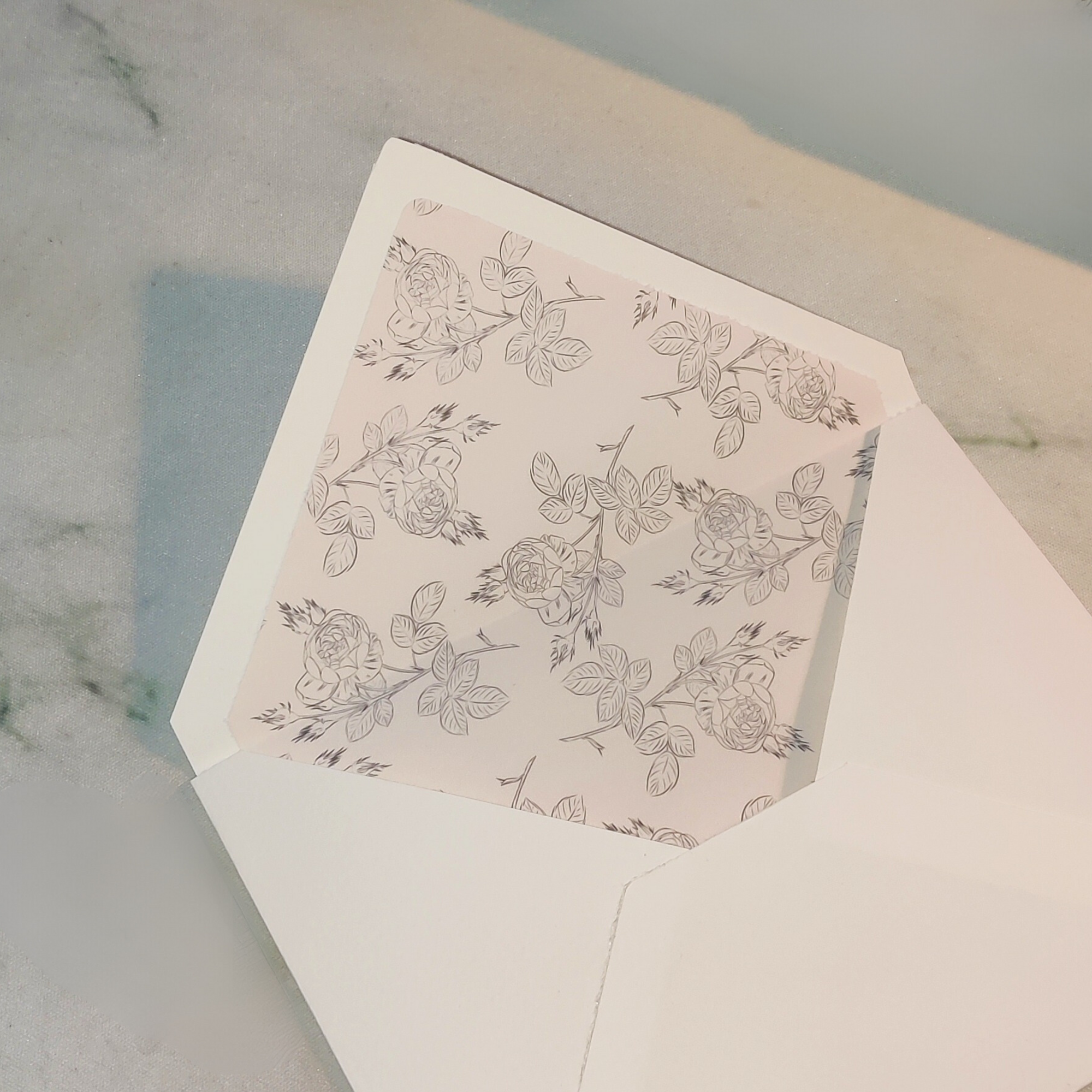 Open white envelope with floral patterned liner showing roses and leaves inside.