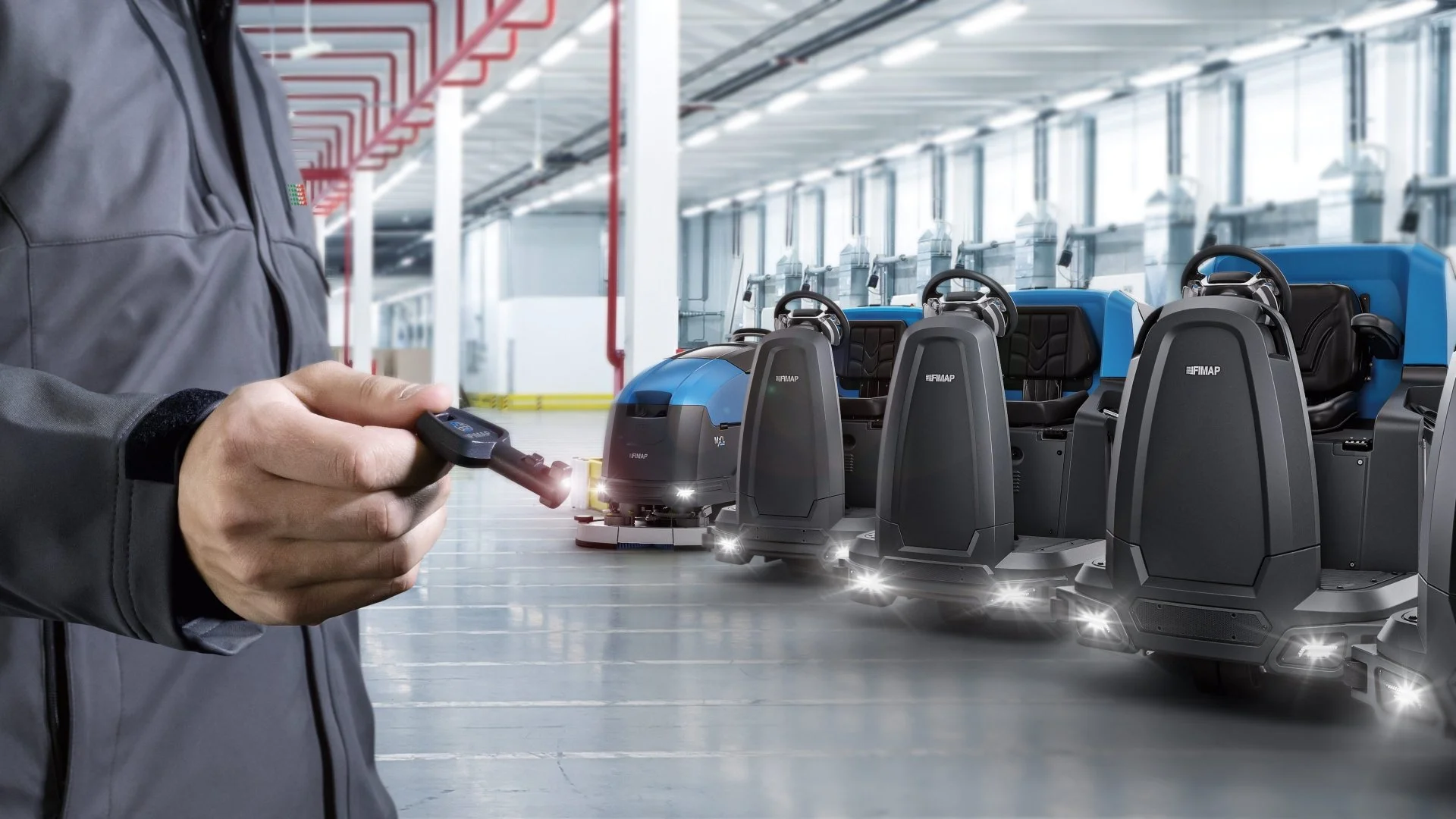 Person holding remote control in warehouse with autonomous robotic floor sweepers parked in background.