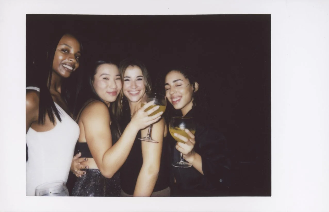 Four women smiling and toasting with cocktails at a party.