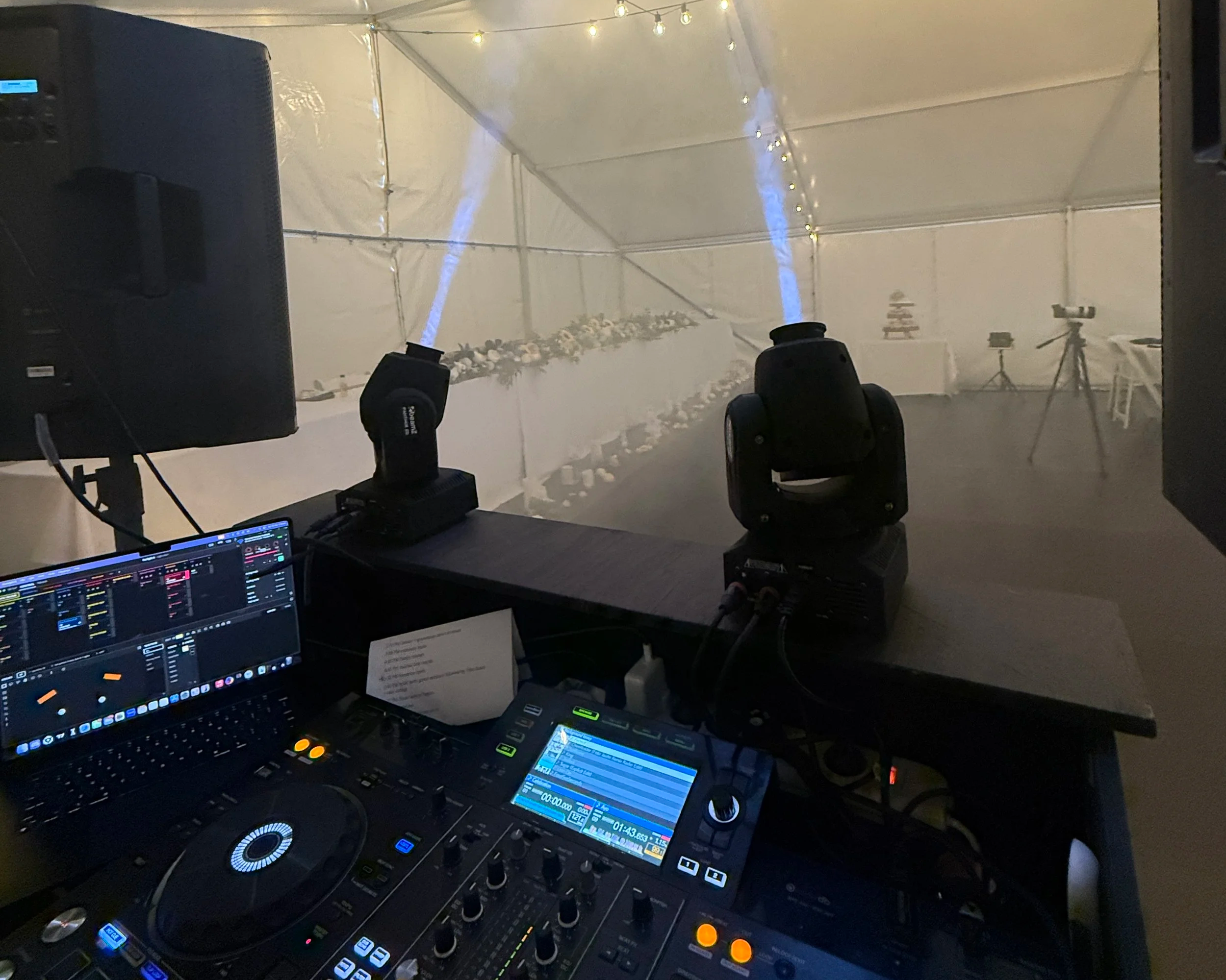 DJ booth with sound mixing equipment, lights, and fog machine, overlooking a decorated event space.